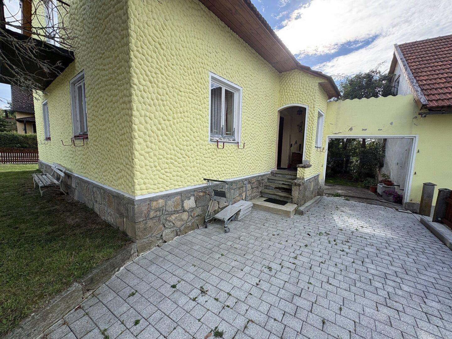 Eingangsbereich des Hauses mit gepflastertem Hof und Steinsockel.