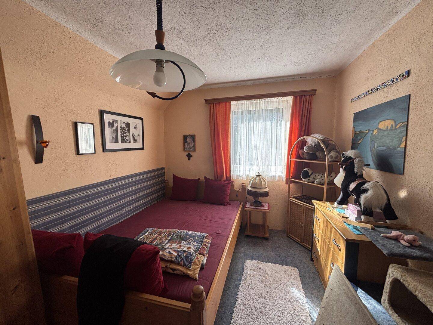 Schlafzimmer mit Einzelbett, Holzmöbeln und orangefarbenen Wänden.