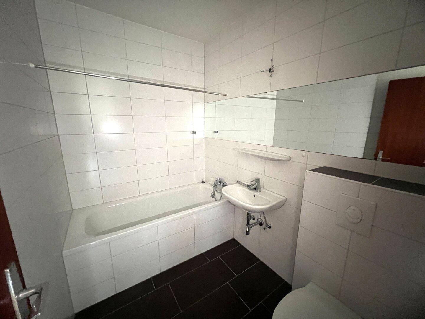 Helles Badezimmer mit weißen Fliesen, Badewanne, Waschbecken und Toilette.