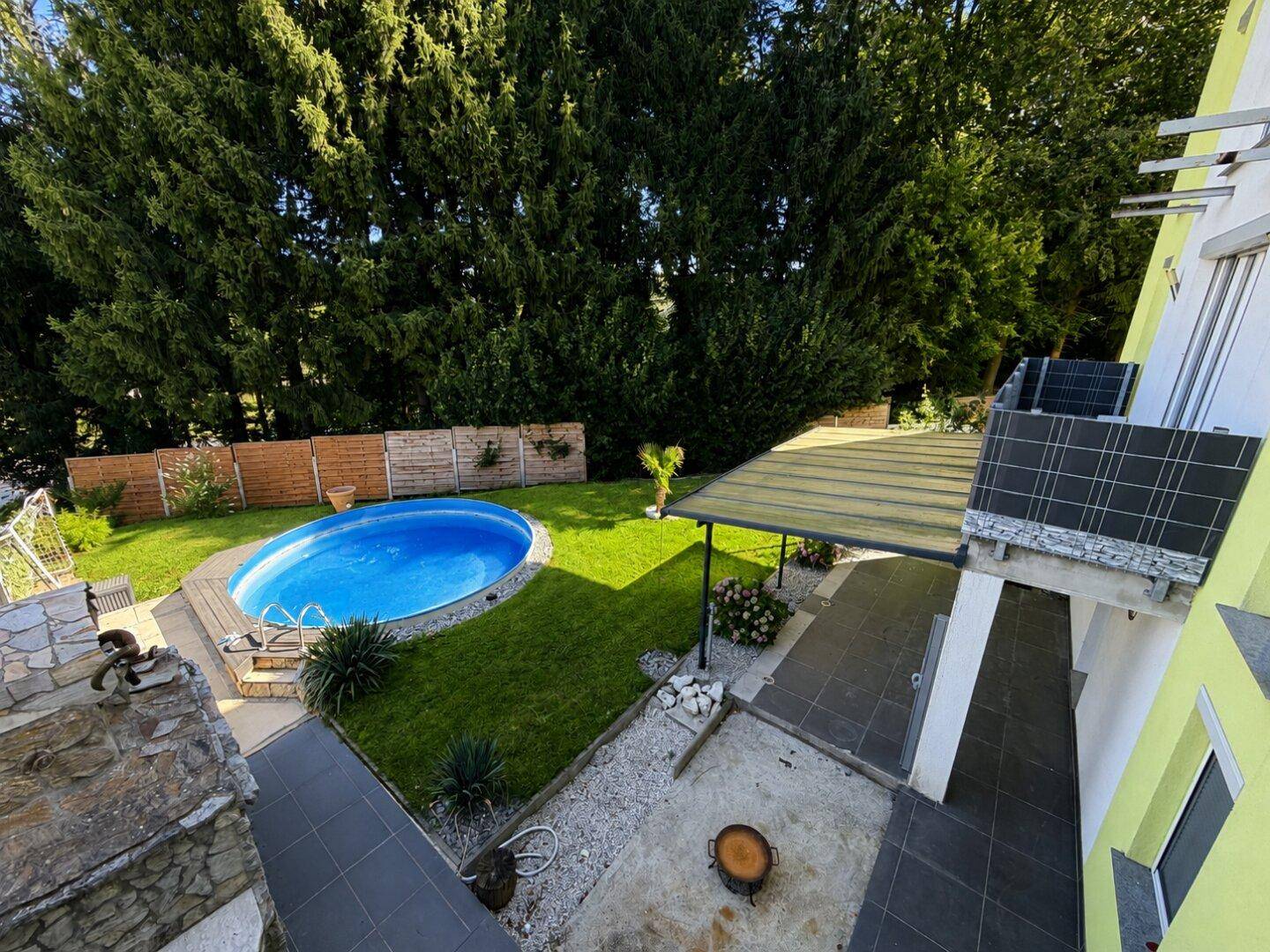 Gepflegter Gartenbereich mit ovalem Pool, Rasenfläche und überdachter Terrasse am Haus.