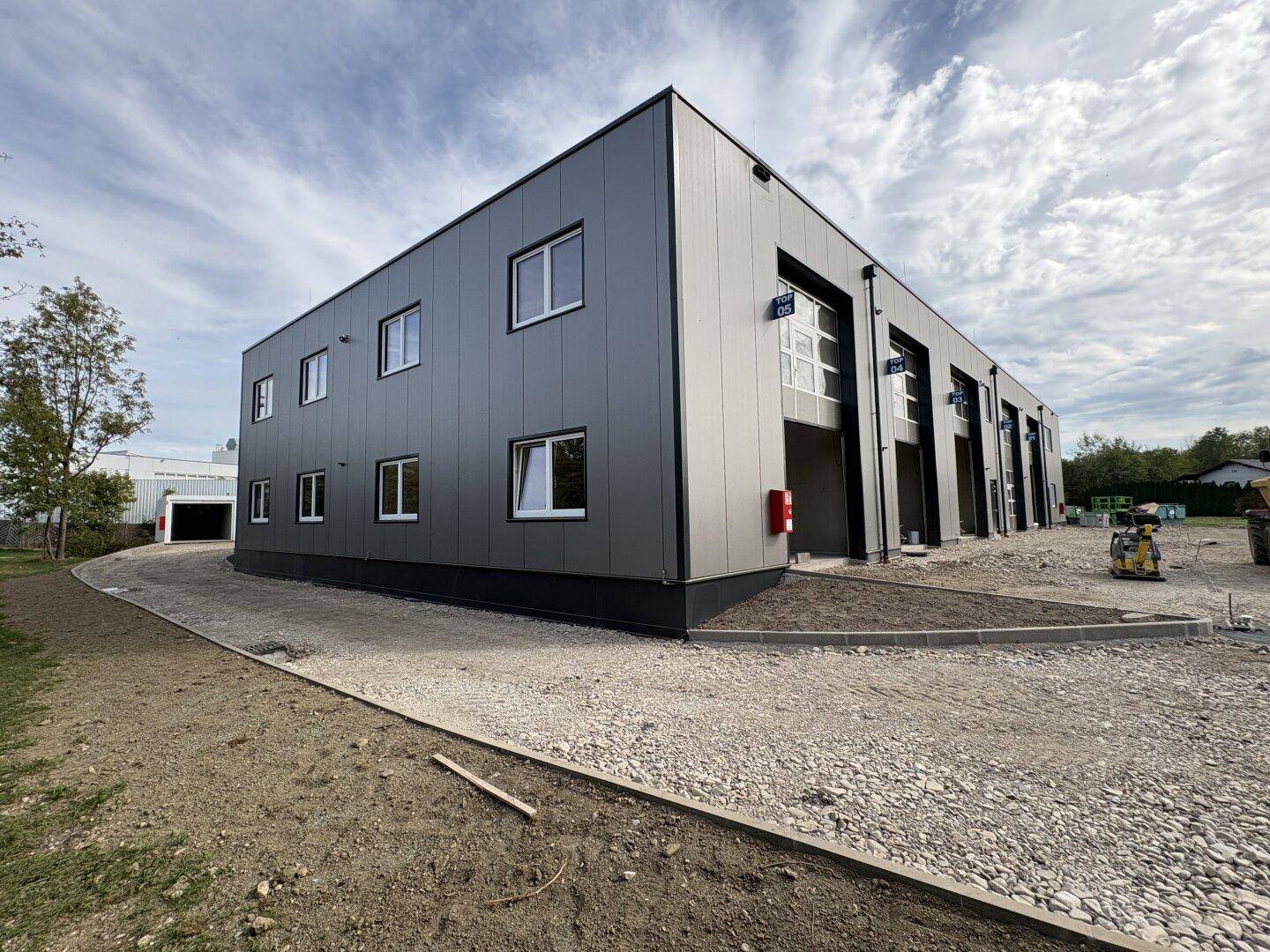Außenansicht eines modernen Gewerbegebäudes im Bau mit grauer Fassade und großen Rolltoren.