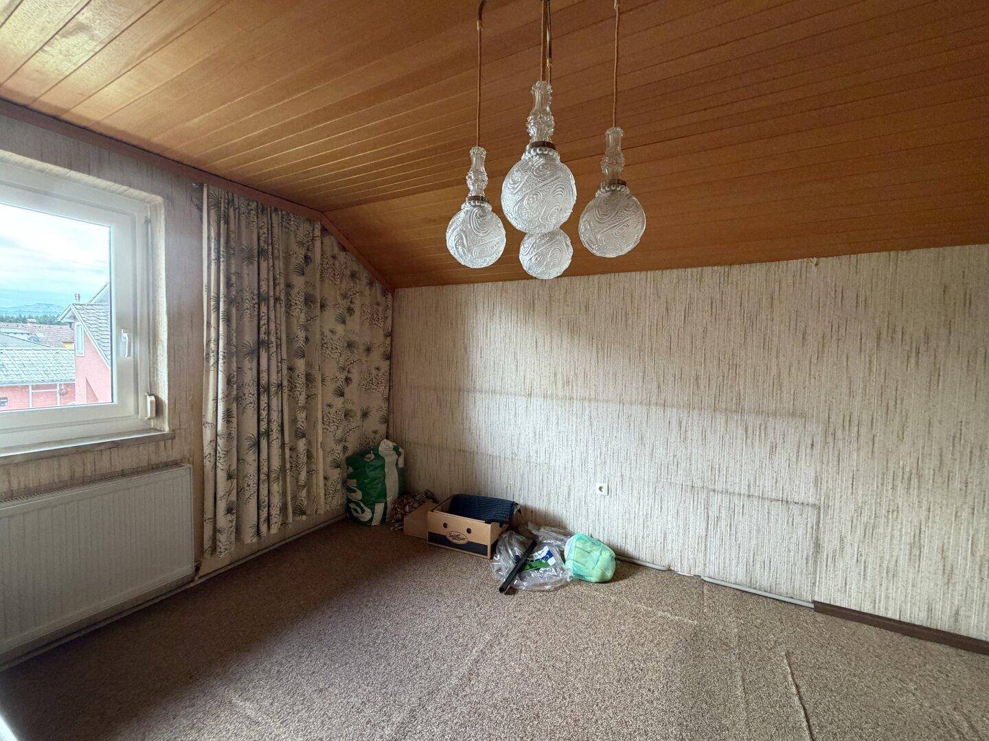 Dachzimmer mit Teppichboden, Holzdecke und schrägen Wänden, bereit zur individuellen Gestaltung.