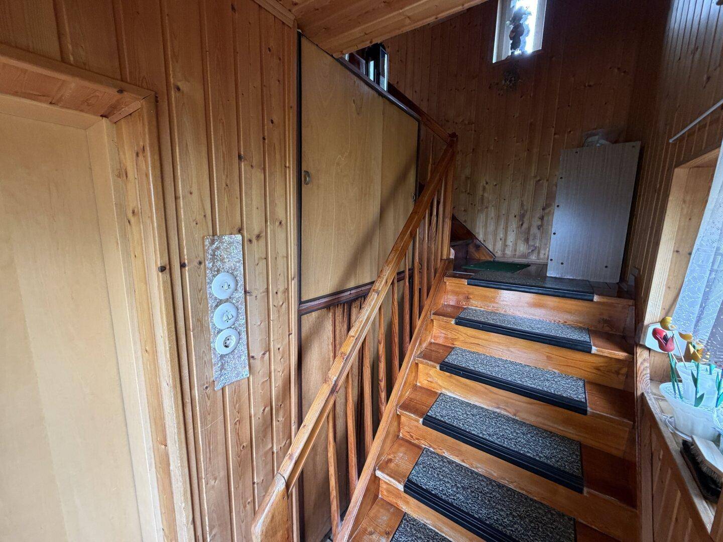 Rustikales Treppenhaus mit Holzverkleidung und Holzgeländer, das die oberen Etagen verbindet.