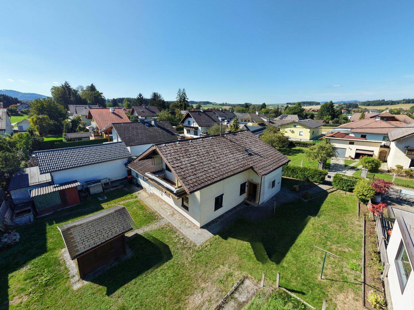 Luftaufnahme eines Einfamilienhauses mit Garten und umliegender Wohnsiedlung in ländlicher Umgebung.