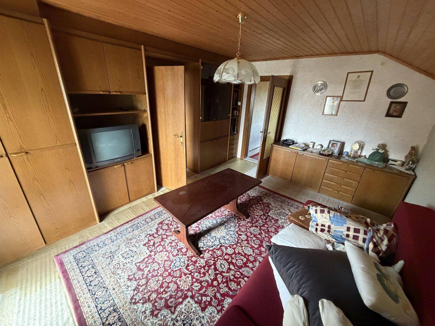 Gemütliches Wohnzimmer im Dachgeschoss mit Holzdecke, Teppich und traditionellen Möbeln.