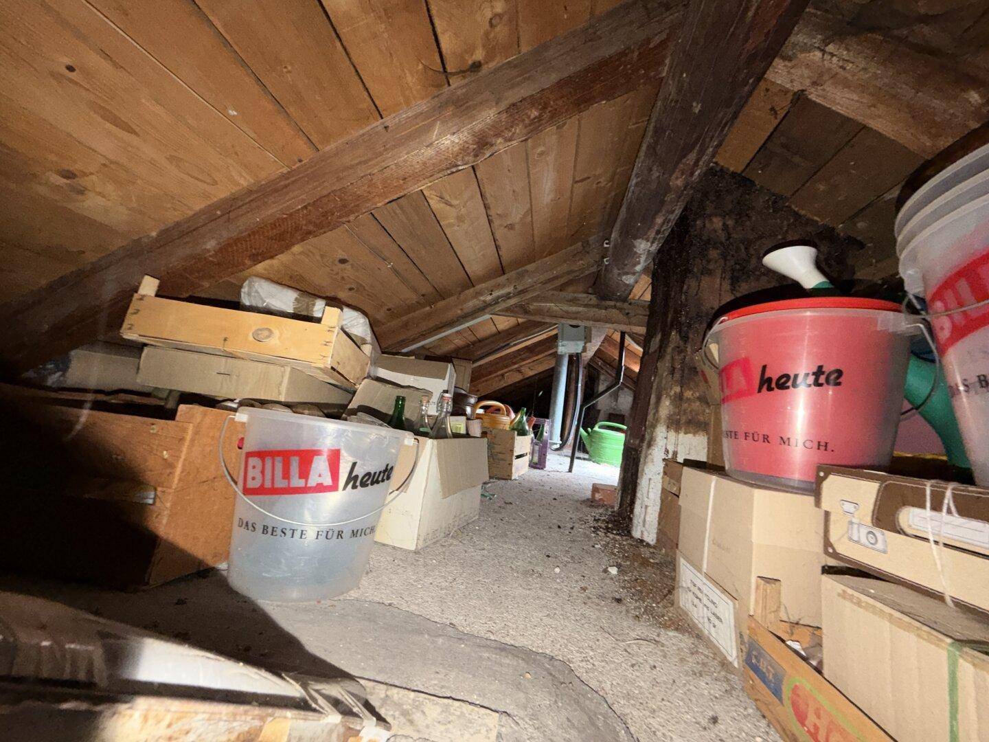 Unausgebauter Dachboden mit sichtbaren Holzbalken, der als Stauraum dient.
