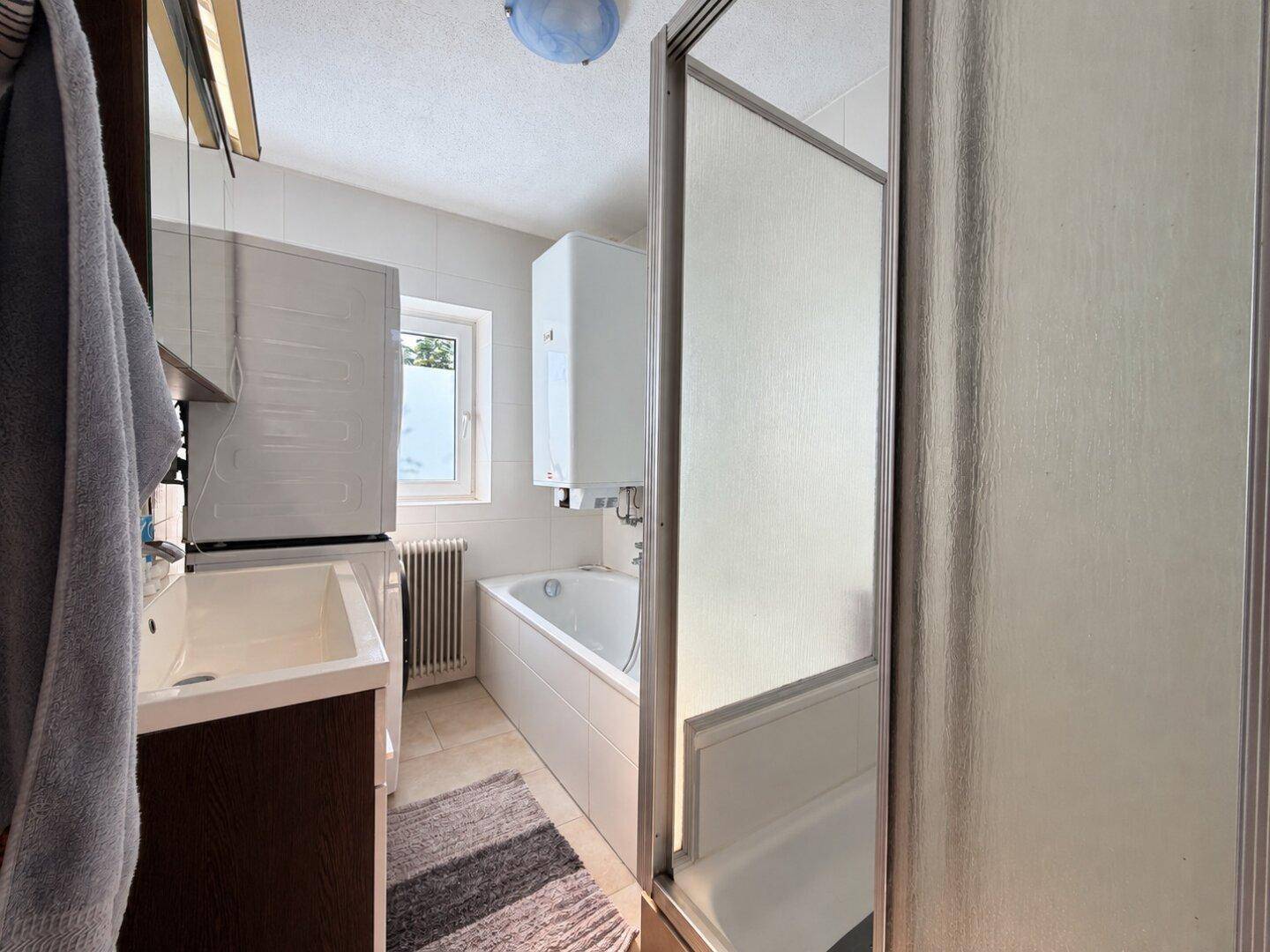 Funktionales Badezimmer mit Badewanne, Dusche, Waschbecken, Waschmaschine und einem Fenster.
