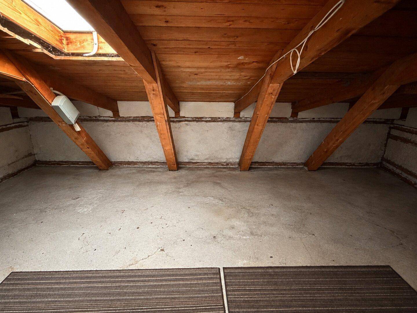 Geräumiger Dachboden mit sichtbaren Holzbalken und einem Betonboden, ideal als Lagerfläche.