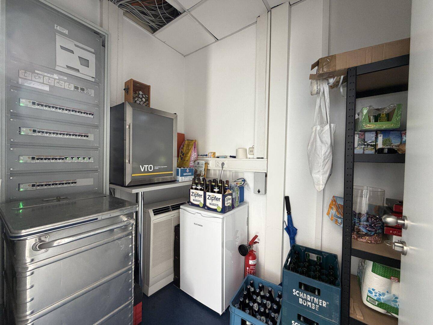 Praktischer Abstellraum mit Kühlschrank, Regalen und elektrischen Schaltkästen für die Gebäudetechnik.