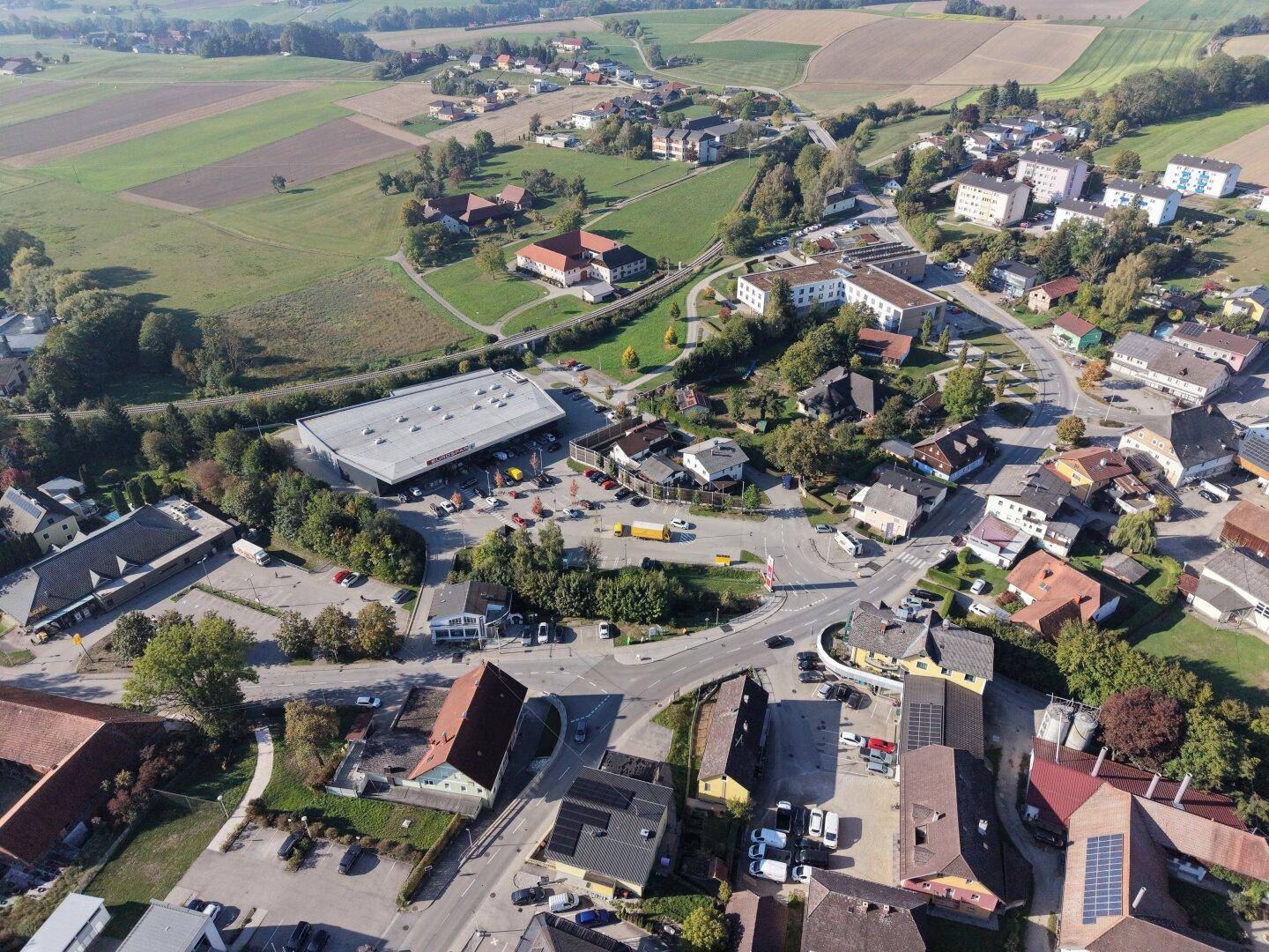 Weitläufige Luftaufnahme einer ländlichen Siedlung mit Feldern und Wäldern in der Umgebung.