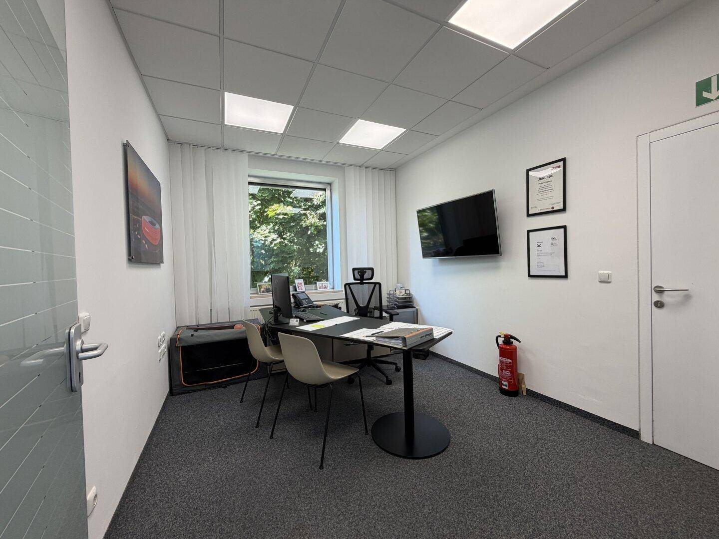 Funktionales Einzelbüro mit Schreibtisch, Bürostuhl, Wandfernseher und Blick ins Grüne.