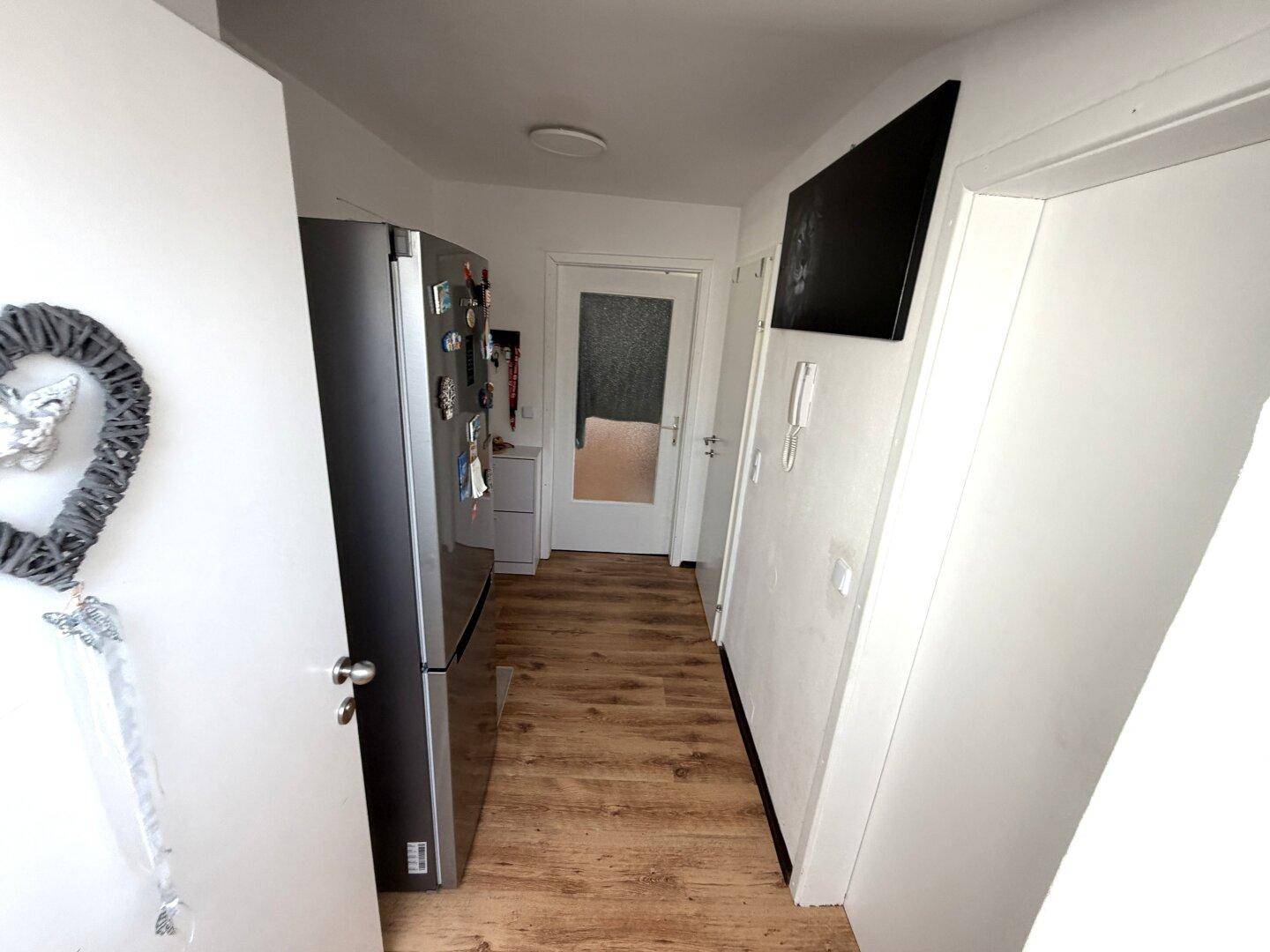 Heller Flur mit Holzboden und einem modernen Kühlschrank, der zu weiteren Räumen führt.