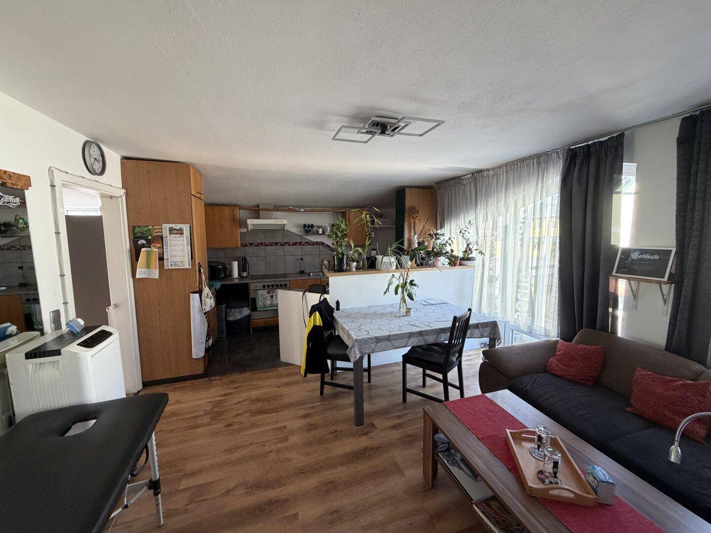 Offener Wohn- und Essbereich mit Holzboden, gemütlichem Sofa und integrierter Küche im Hintergrund.