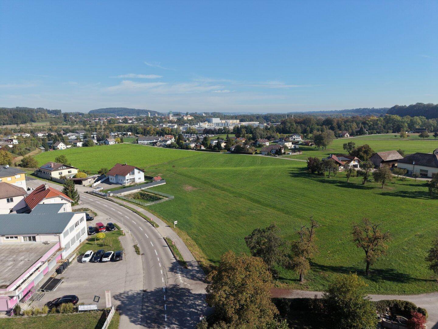 Weitläufige Luftaufnahme einer ländlichen Gegend mit grünen Feldern, Häusern und bewaldeten Hügeln im Hintergrund.