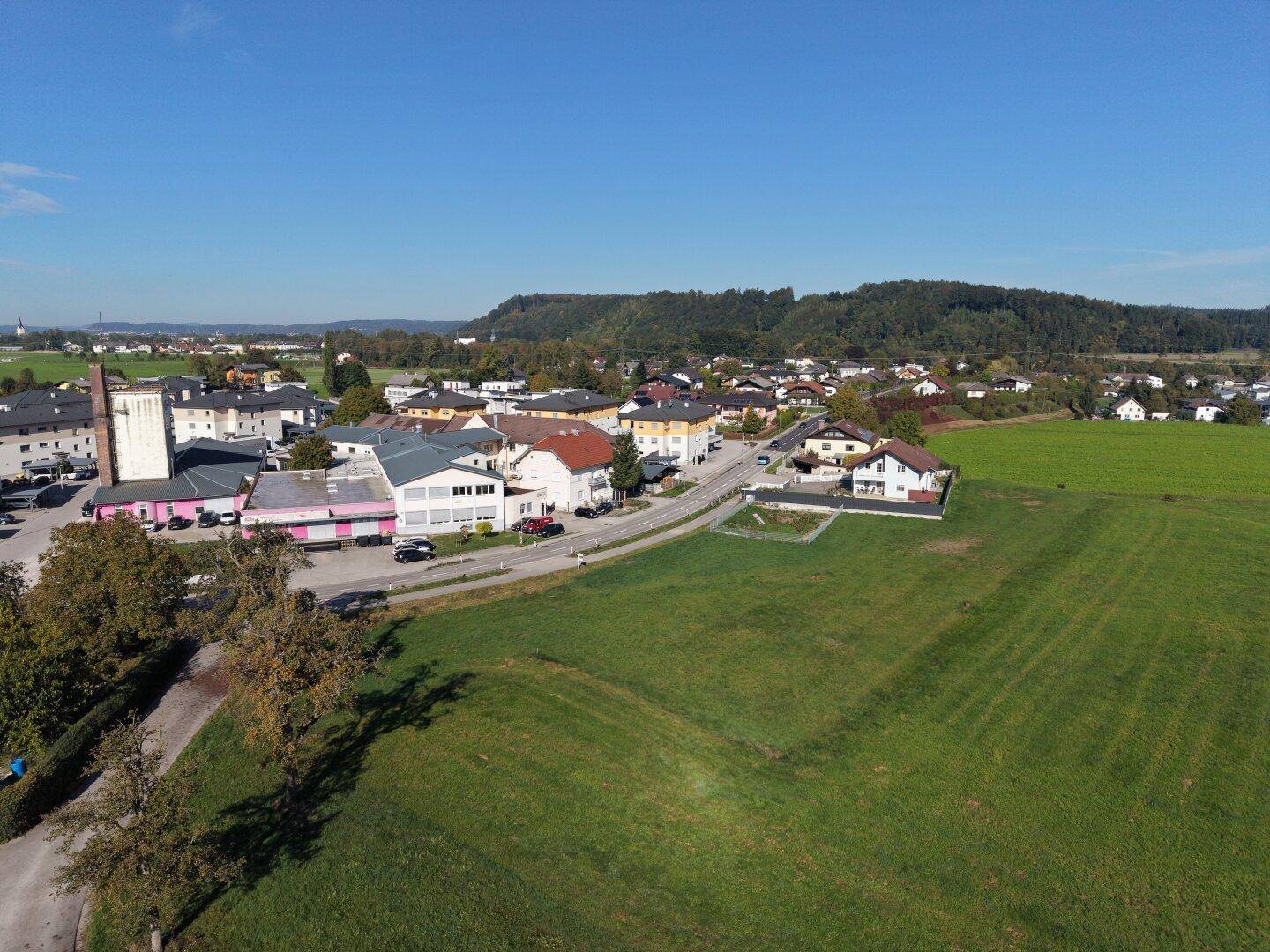 Panoramablick aus der Vogelperspektive auf eine Siedlung umgeben von weiten Grünflächen und einem klaren Himmel.