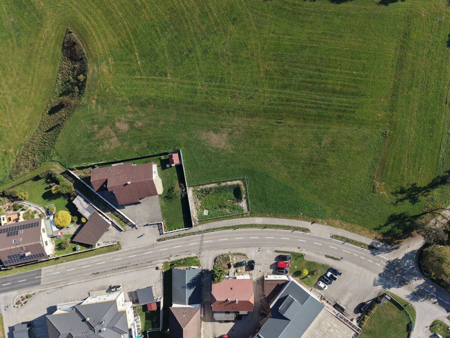 Senkrechte Luftaufnahme einer Straße, umgeben von Wohngebäuden und weitläufigen grünen Feldern.