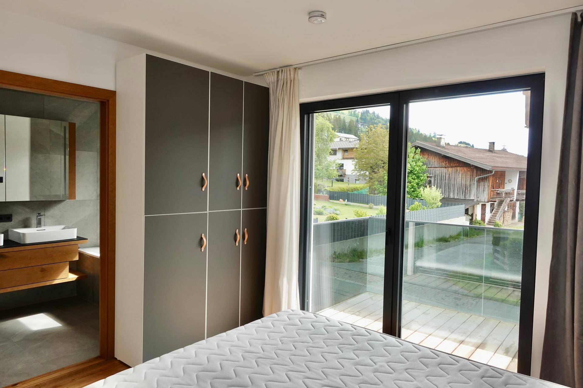 Schlafzimmer mit Einbauschränken, Balkonzugang und Blick ins Grüne mit angrenzendem Bad.