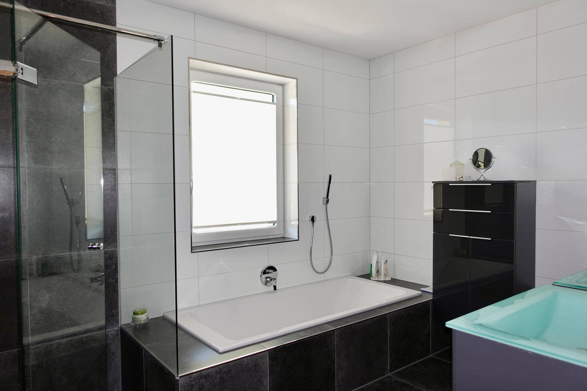 Badezimmer mit Badewanne, Dusche und weißen sowie dunklen Fliesen.