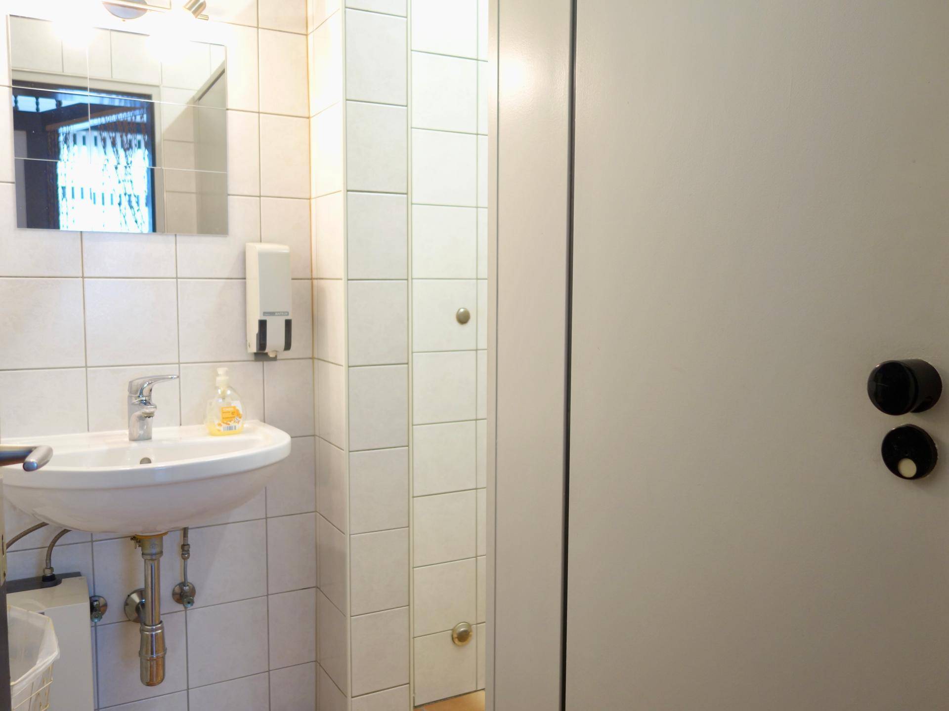 Waschbeckenbereich in einer Toilette mit weißen Fliesen und einem Seifenspender an der Wand.