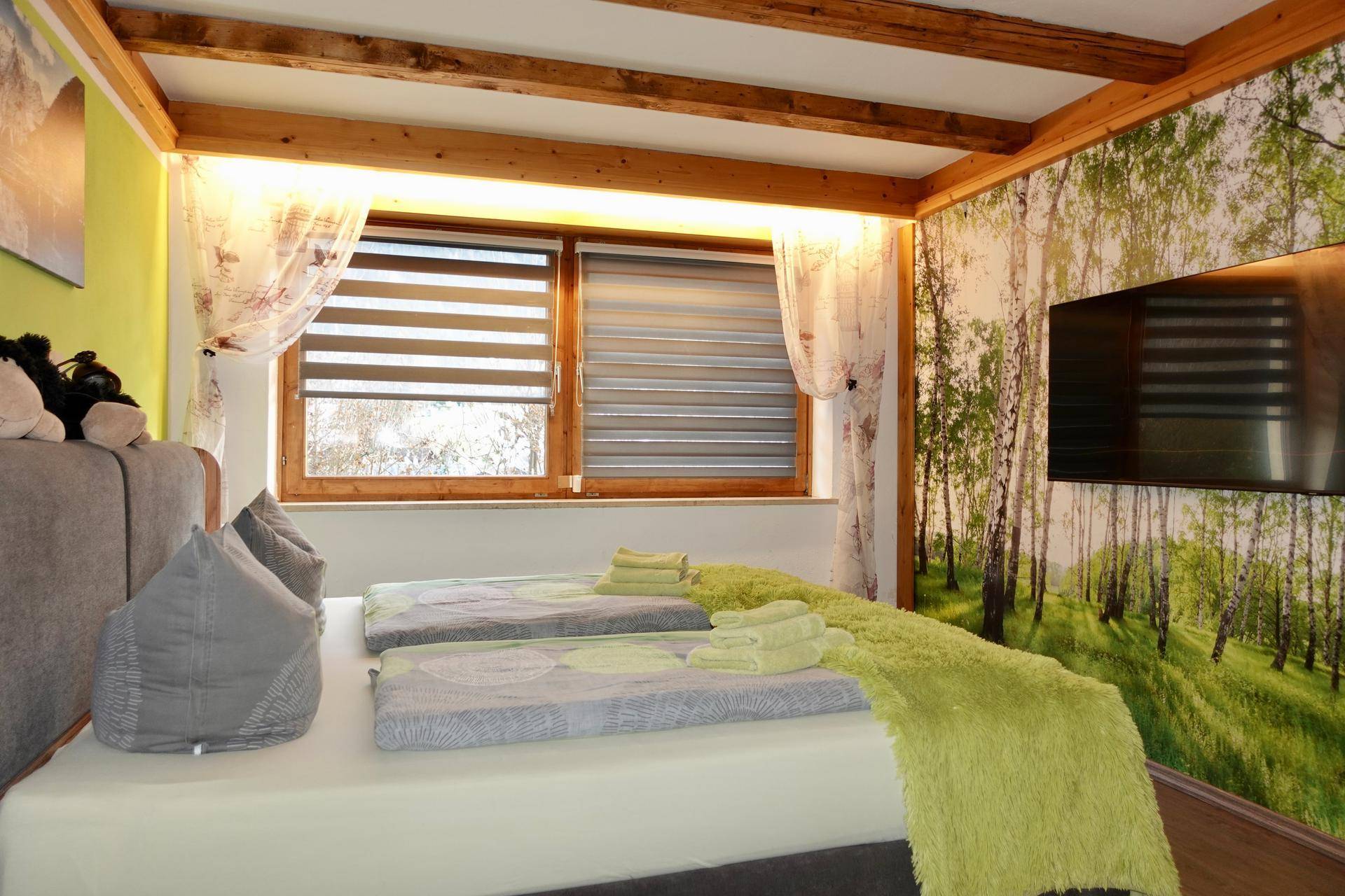Schlafzimmer mit Holzbalken, Doppelbett und Waldmotiv-Tapete.