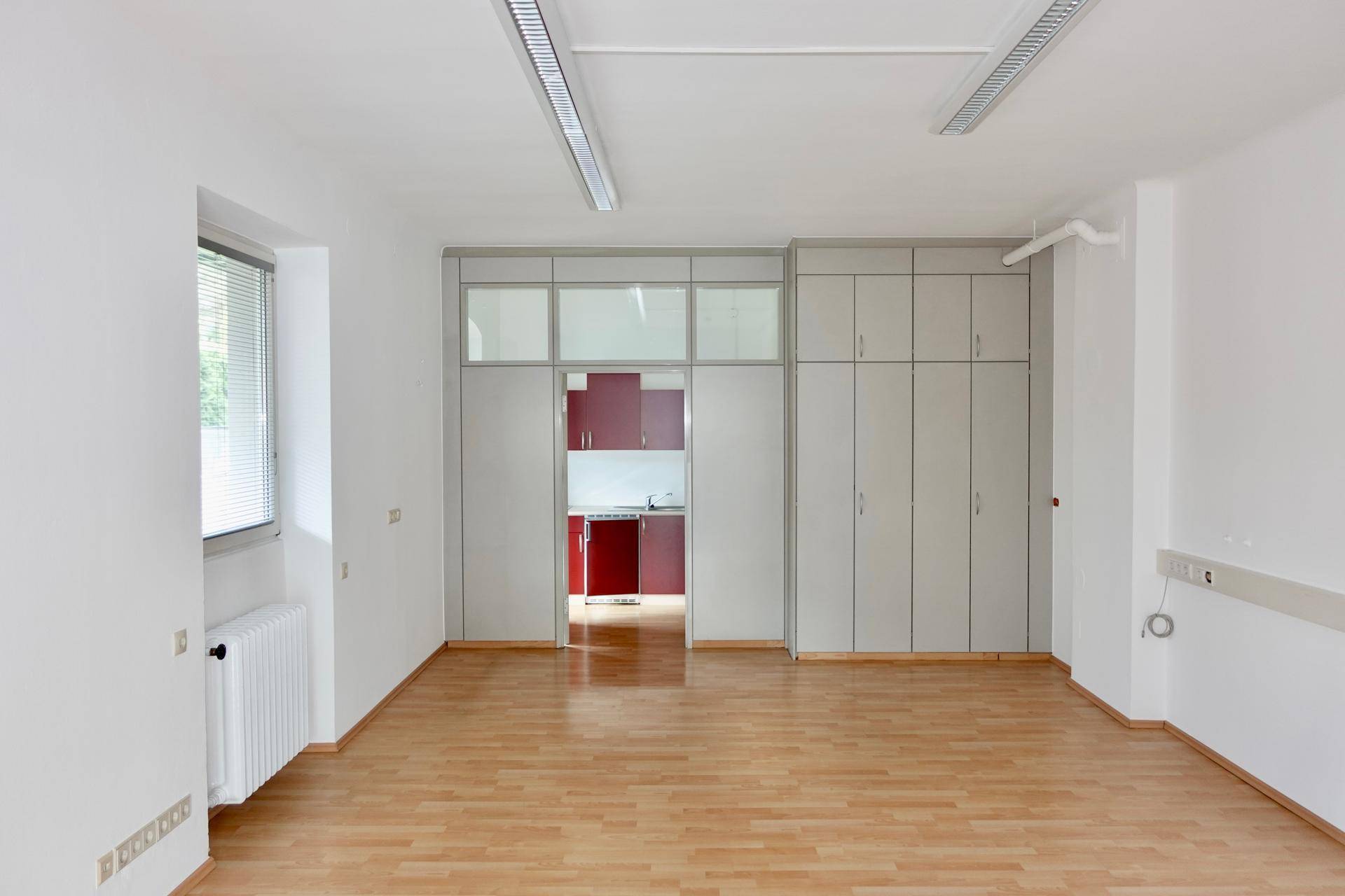 Großer Büroraum mit Einbauschränken und Zugang zu einer kleinen, roten Küchenzeile.