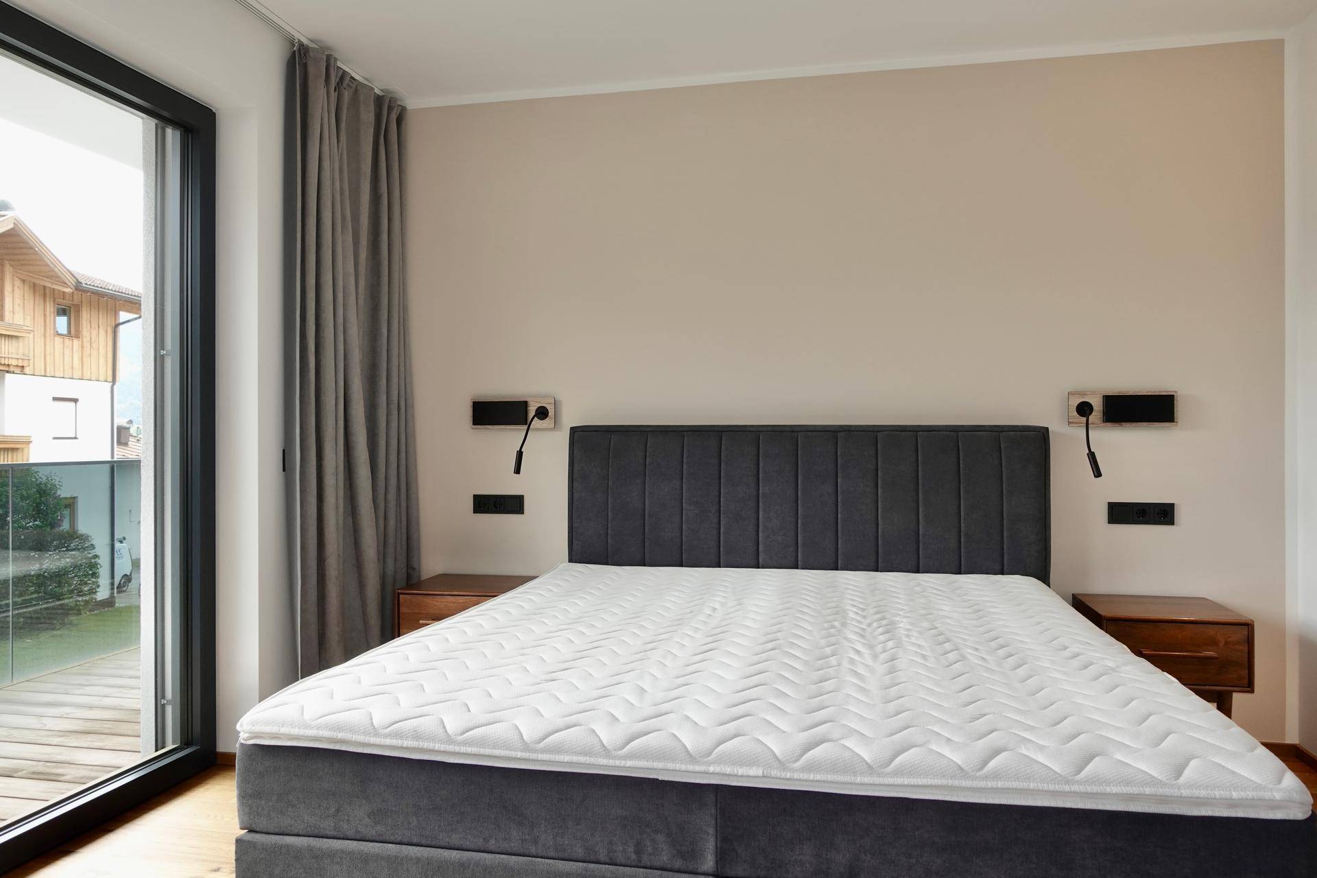 Helles Schlafzimmer mit großem Bett, Holzboden und Zugang zu einem Außenbereich.
