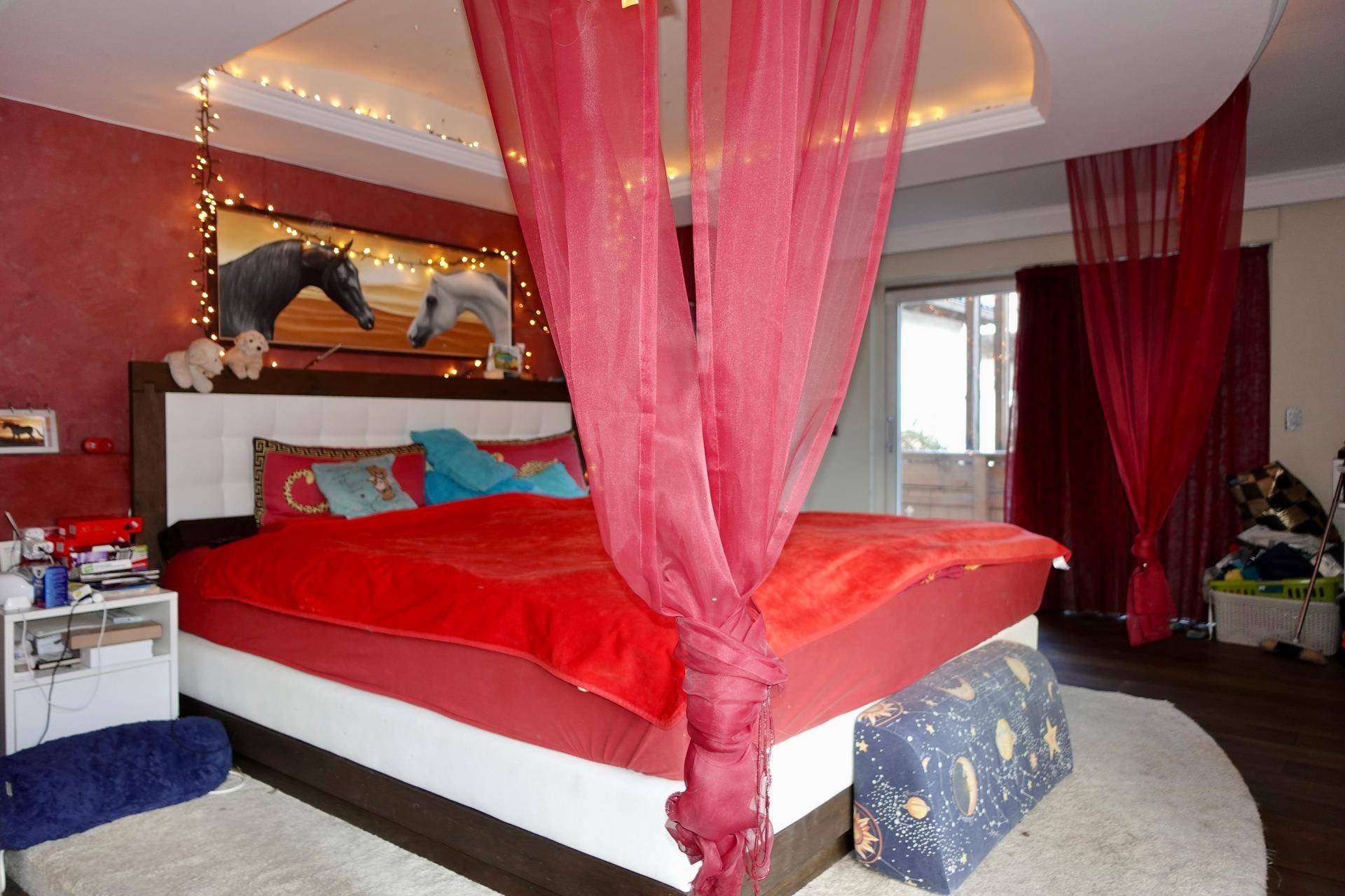 Romantisches Schlafzimmer mit Himmelbett, roten Akzenten und indirekter Beleuchtung.