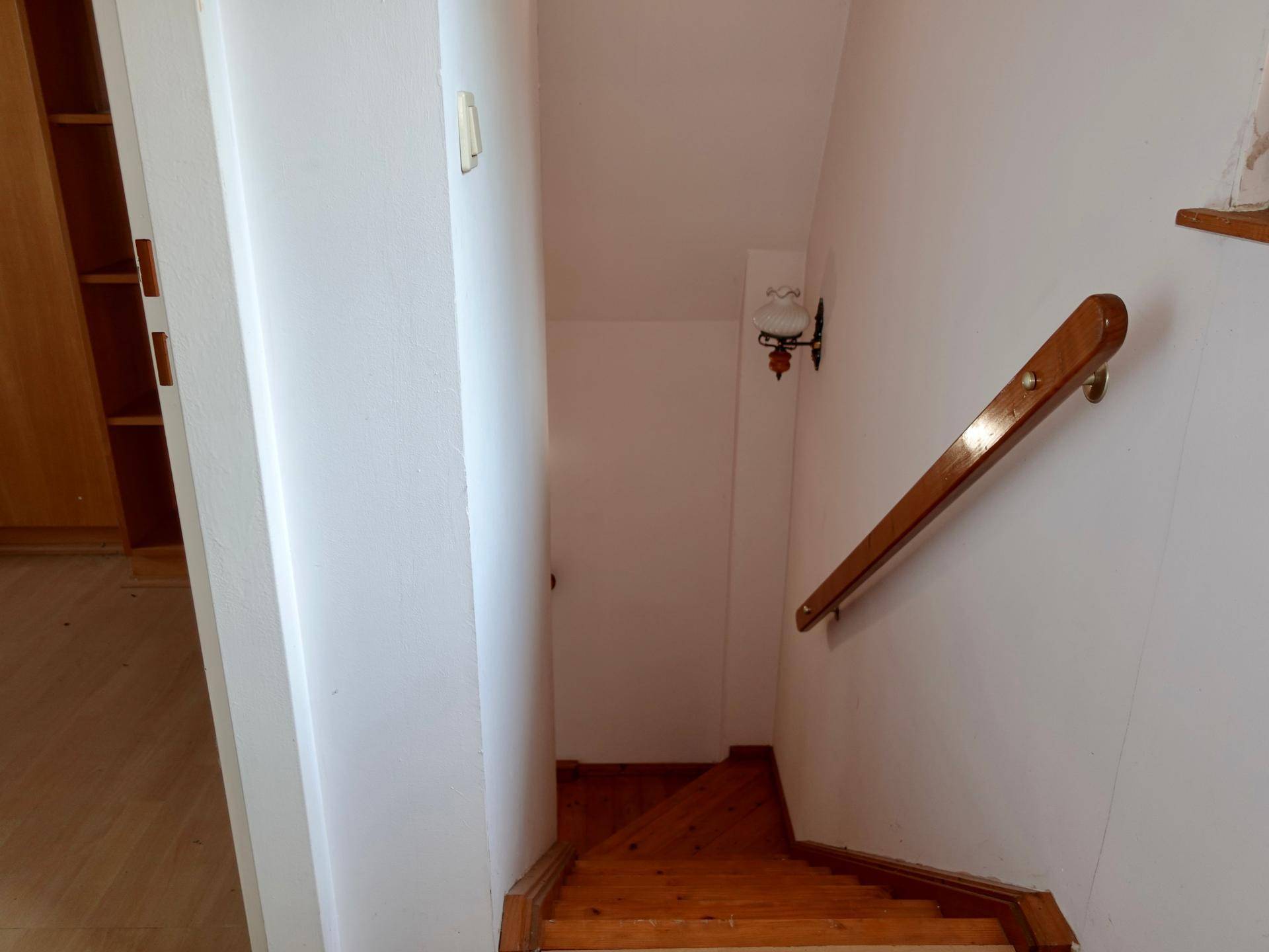 Holztreppe mit Geländer führt in das obere Stockwerk, helle Wände.
