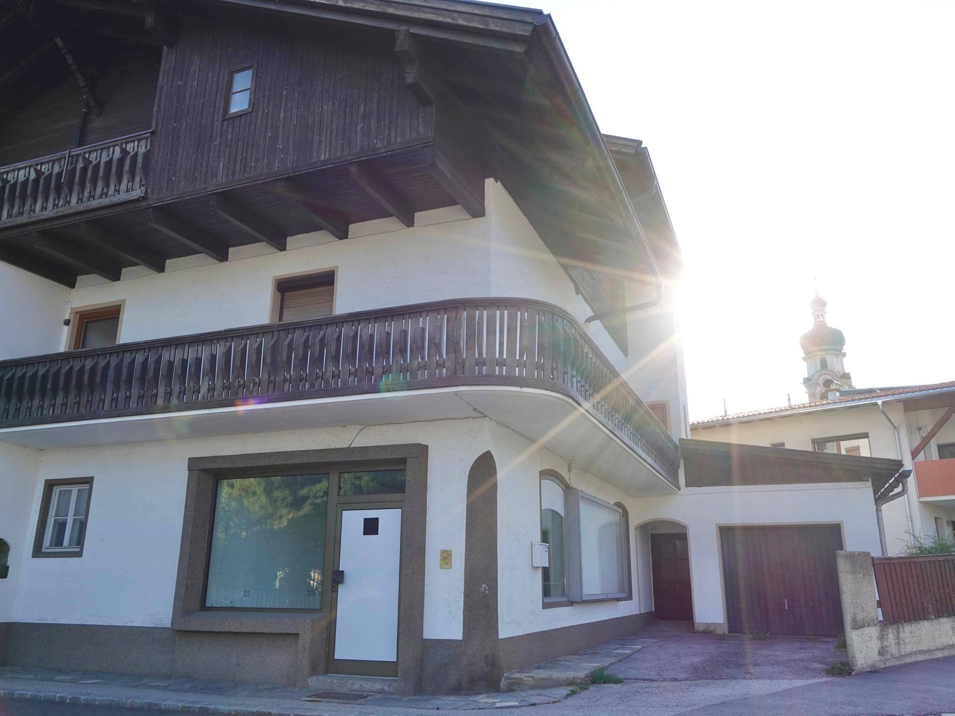 Außenansicht des traditionellen Gebäudes mit Holzbalkonen und Ladenlokal, beleuchtet von der strahlenden Morgensonne.