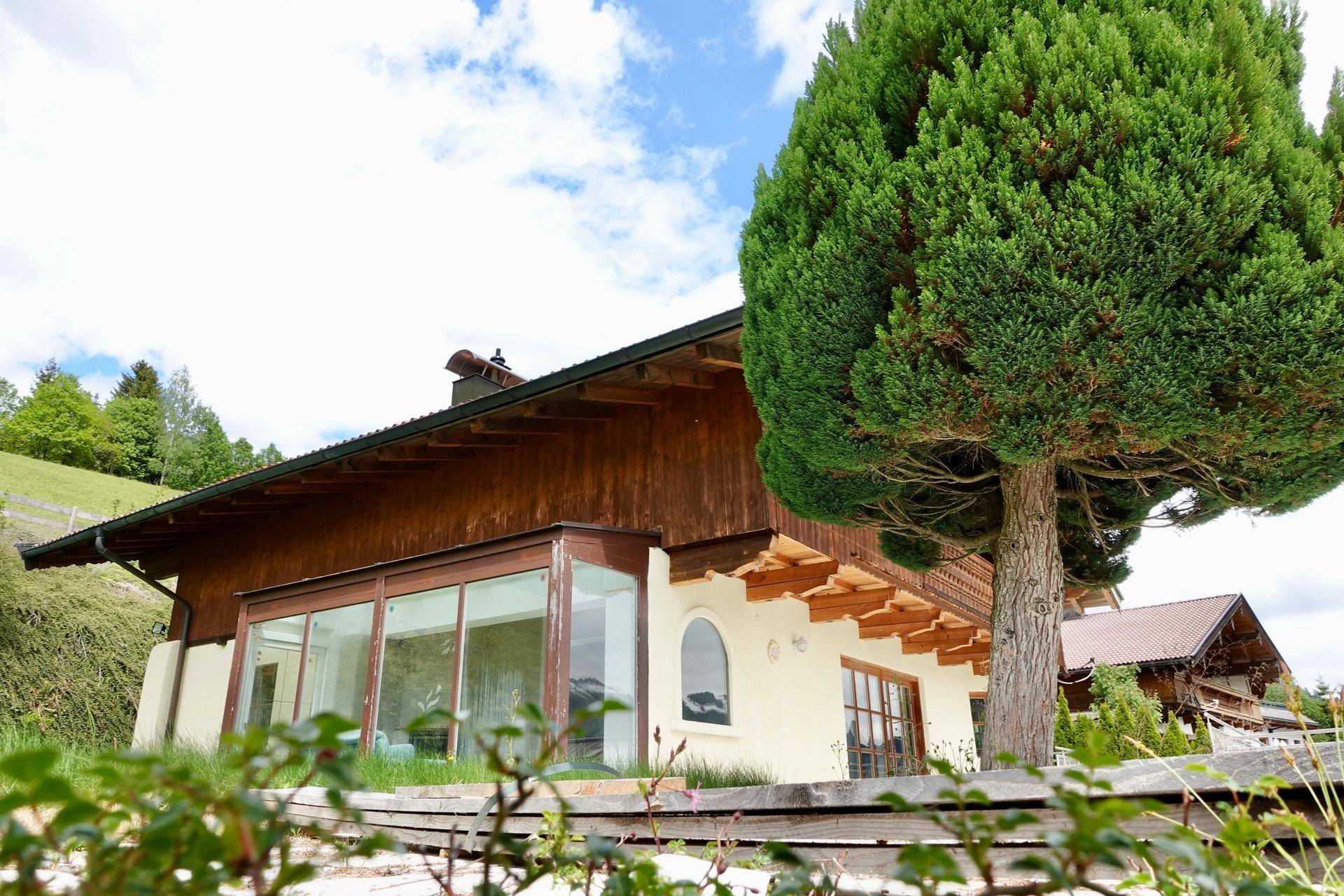 Seitenansicht des Hauses mit großen Fenstern und traditionellen Holzelementen.