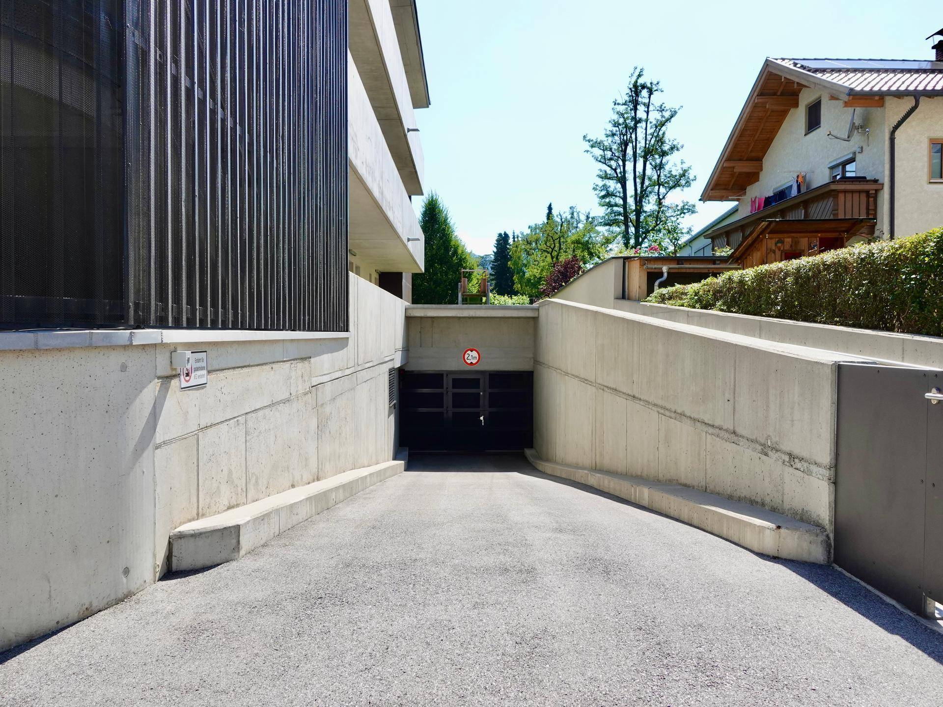 Zufahrt zu einer Tiefgarage mit Betonwänden und Höhenbegrenzungsschild, umgeben von Wohngebäuden.