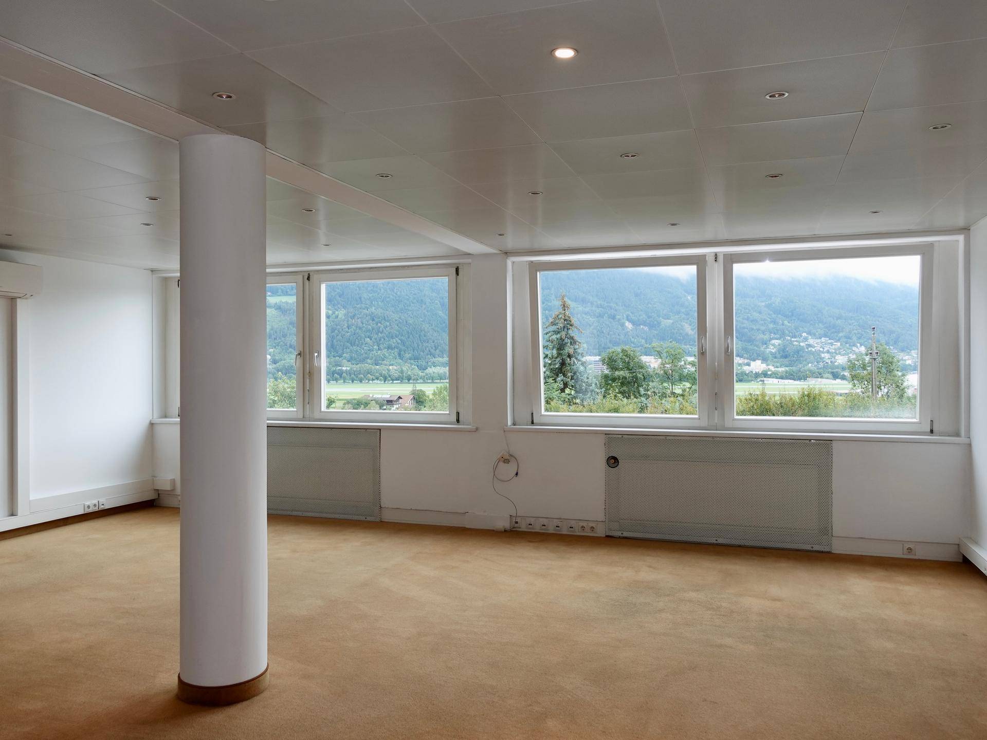 Heller Büroraum mit Teppichboden, Einbaustrahlern und weitem Blick auf die Landschaft.