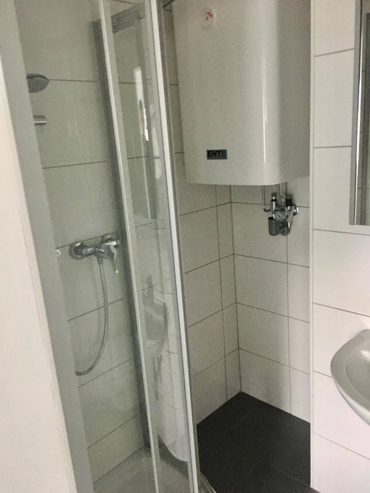 Modernes Badezimmer mit Duschkabine, weiß gefliesten Wänden und einem Warmwasserboiler.
