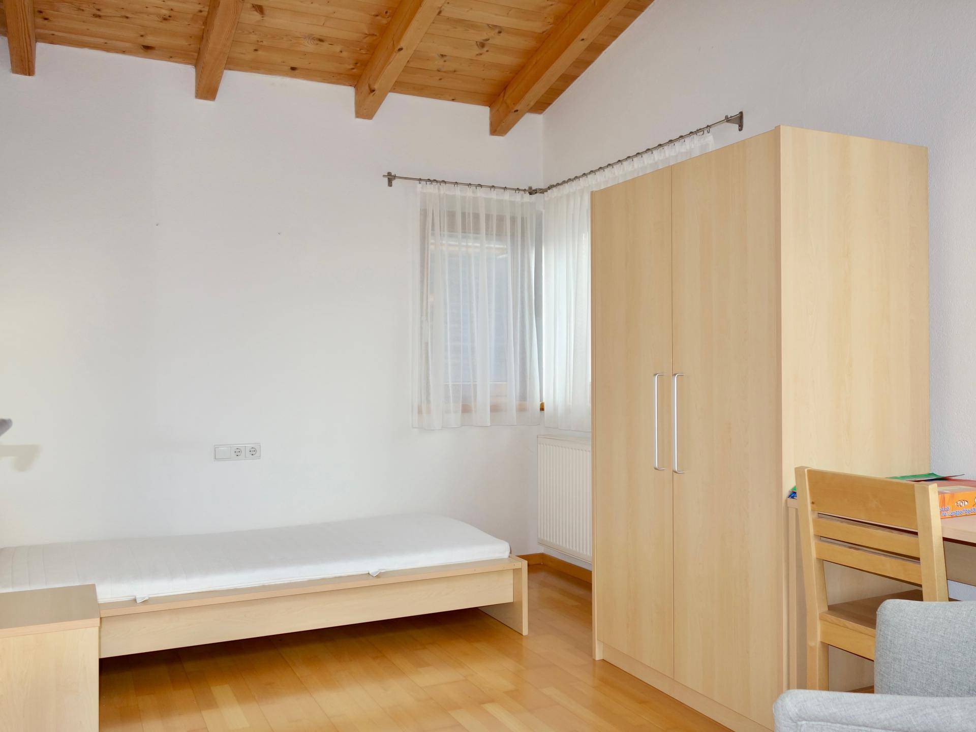 Schlafzimmer mit Holzboden, Dachschräge und Fenster, ausgestattet mit einem Einzelbett.