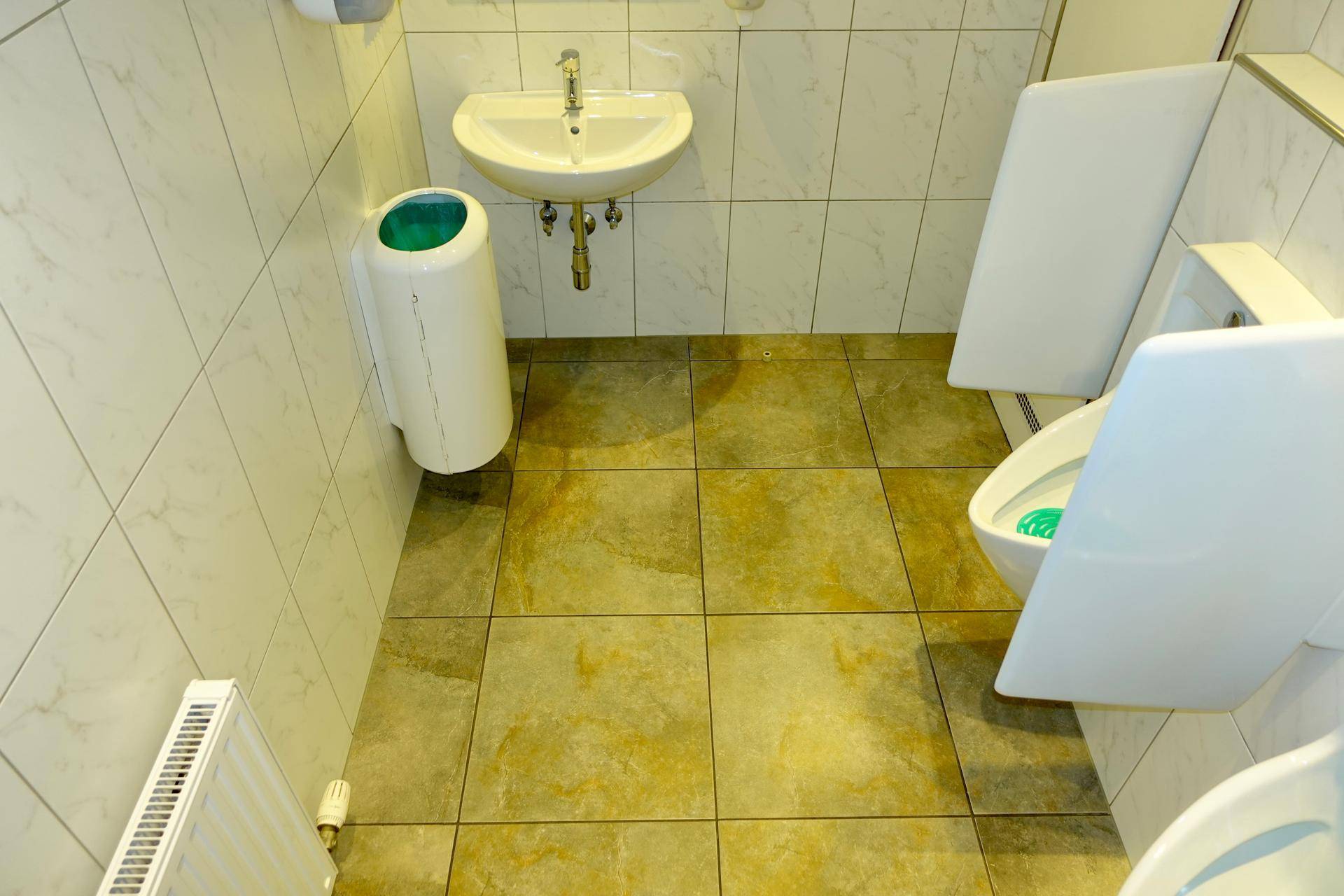 Eine saubere Herrentoilette mit Fliesenboden, Waschbecken und Urinalen, ausgestattet mit einem Heizkörper.
