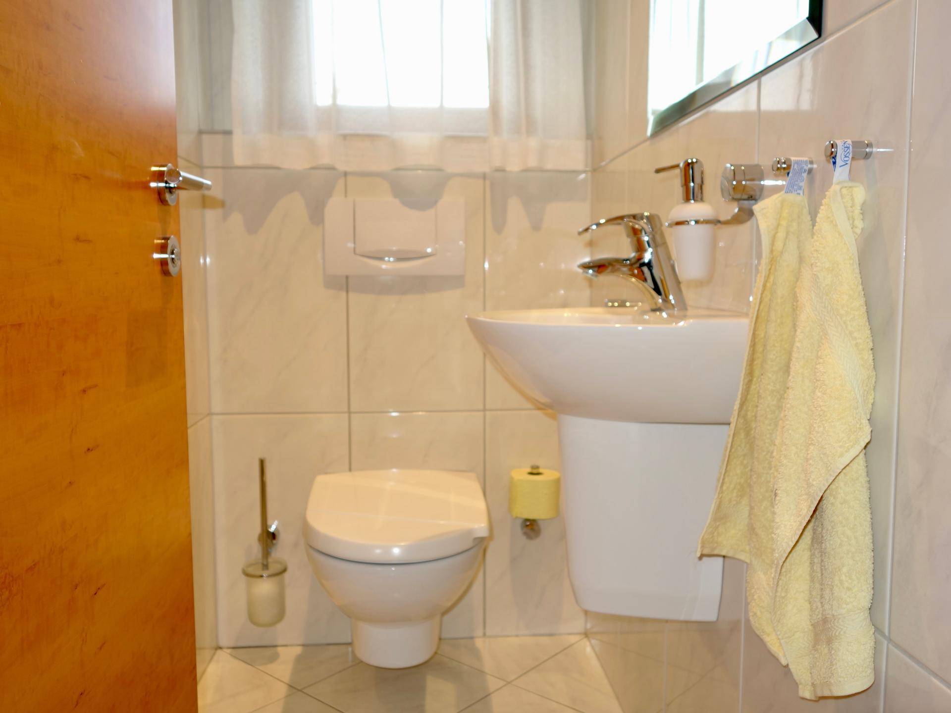 Kleines Gäste-WC mit wandhängendem WC, Waschbecken und Fenster für Tageslicht.