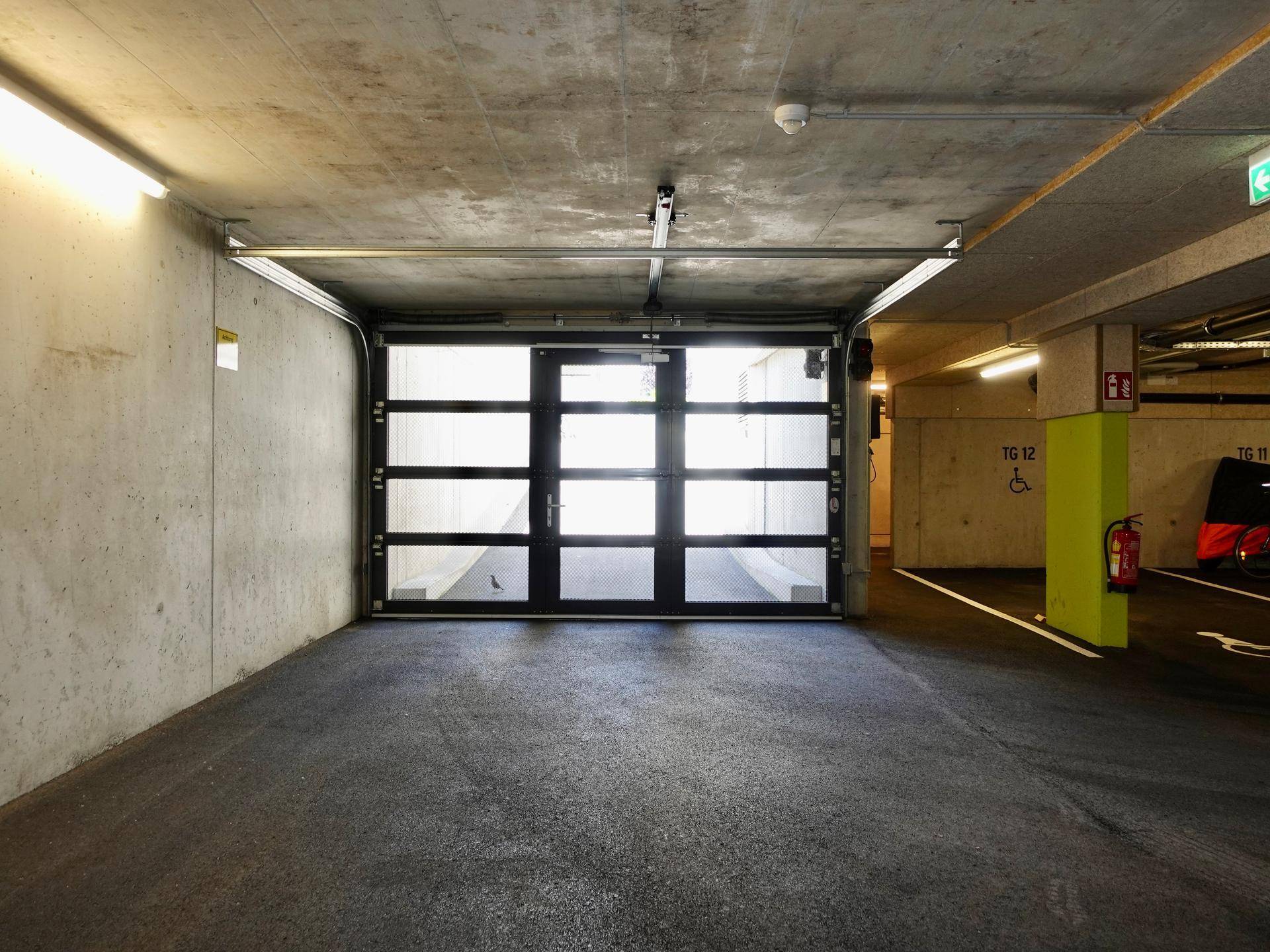 Eingangsbereich einer Tiefgarage mit moderner Glas-Garagentür und Betonwänden.
