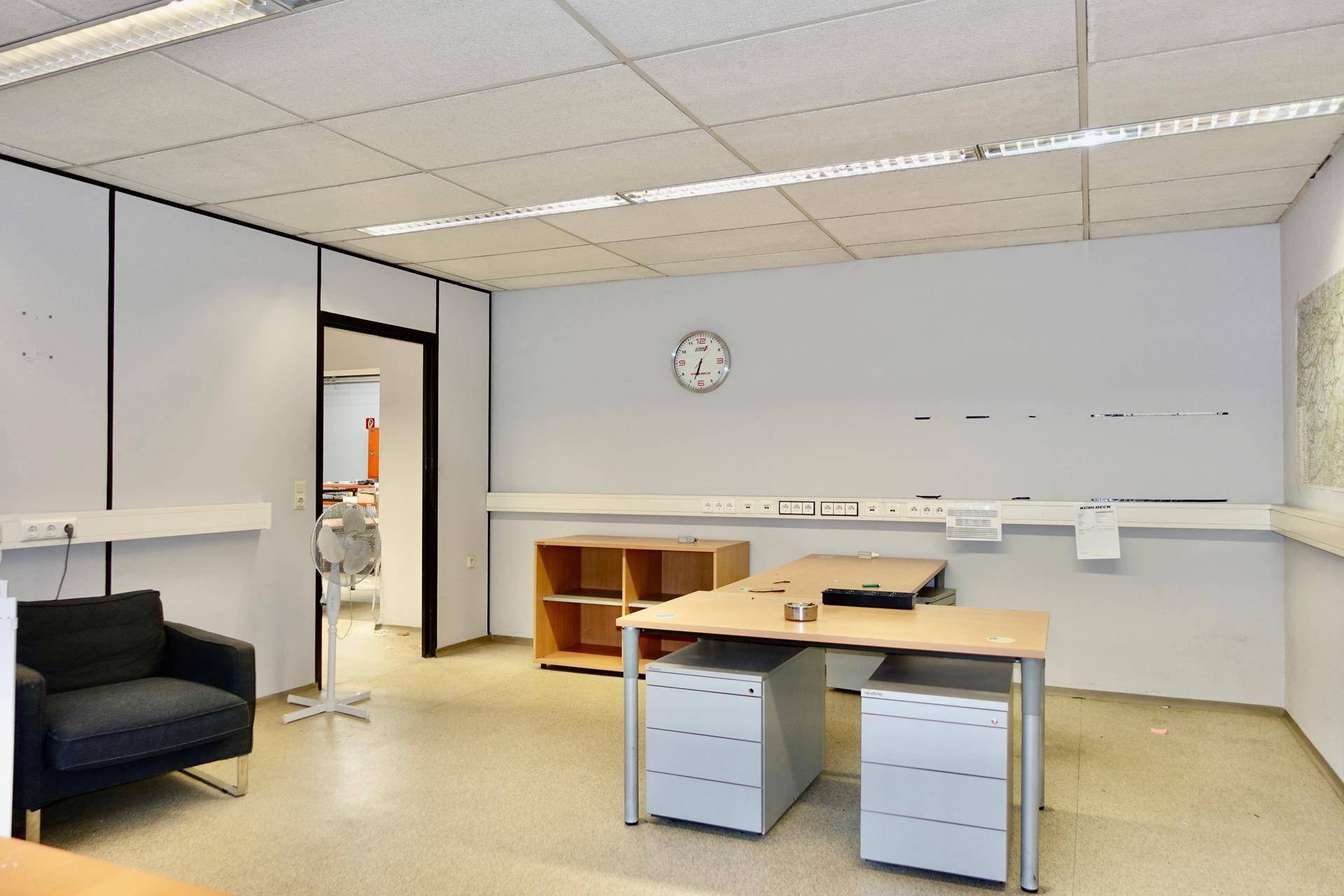 Helles Büro mit modularen Trennwänden, Schreibtischen und einem Sessel, bereit zur Nutzung.