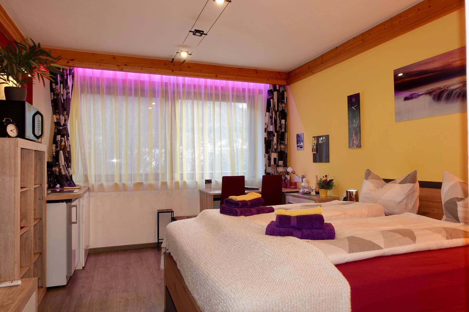 Helles Schlafzimmer mit Doppelbett, Holzbalken und farbiger Beleuchtung.