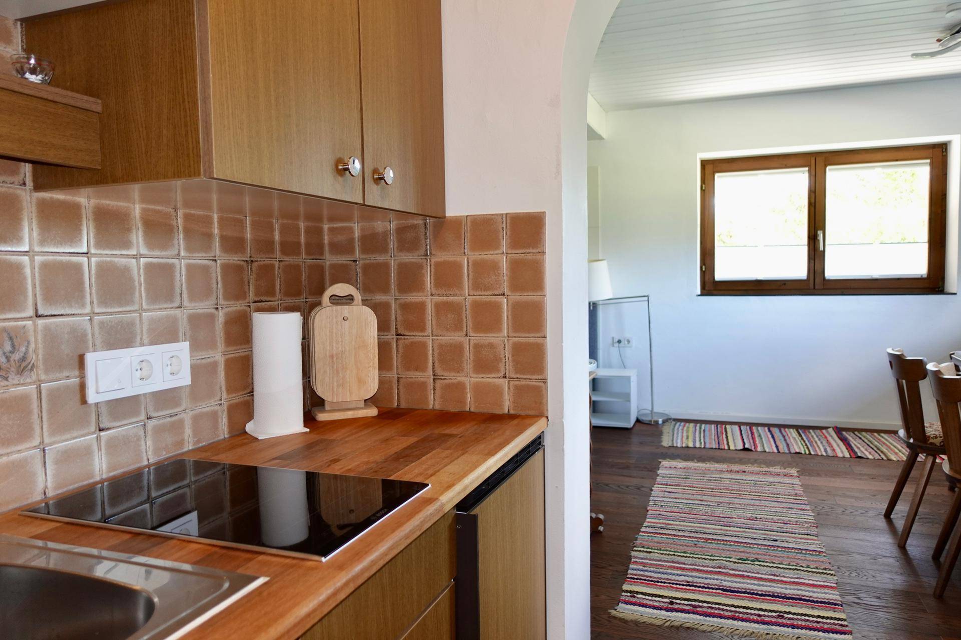 Kleine Küche mit Holztheke, braunen Fliesen und Induktionskochfeld, offen zum Essbereich.