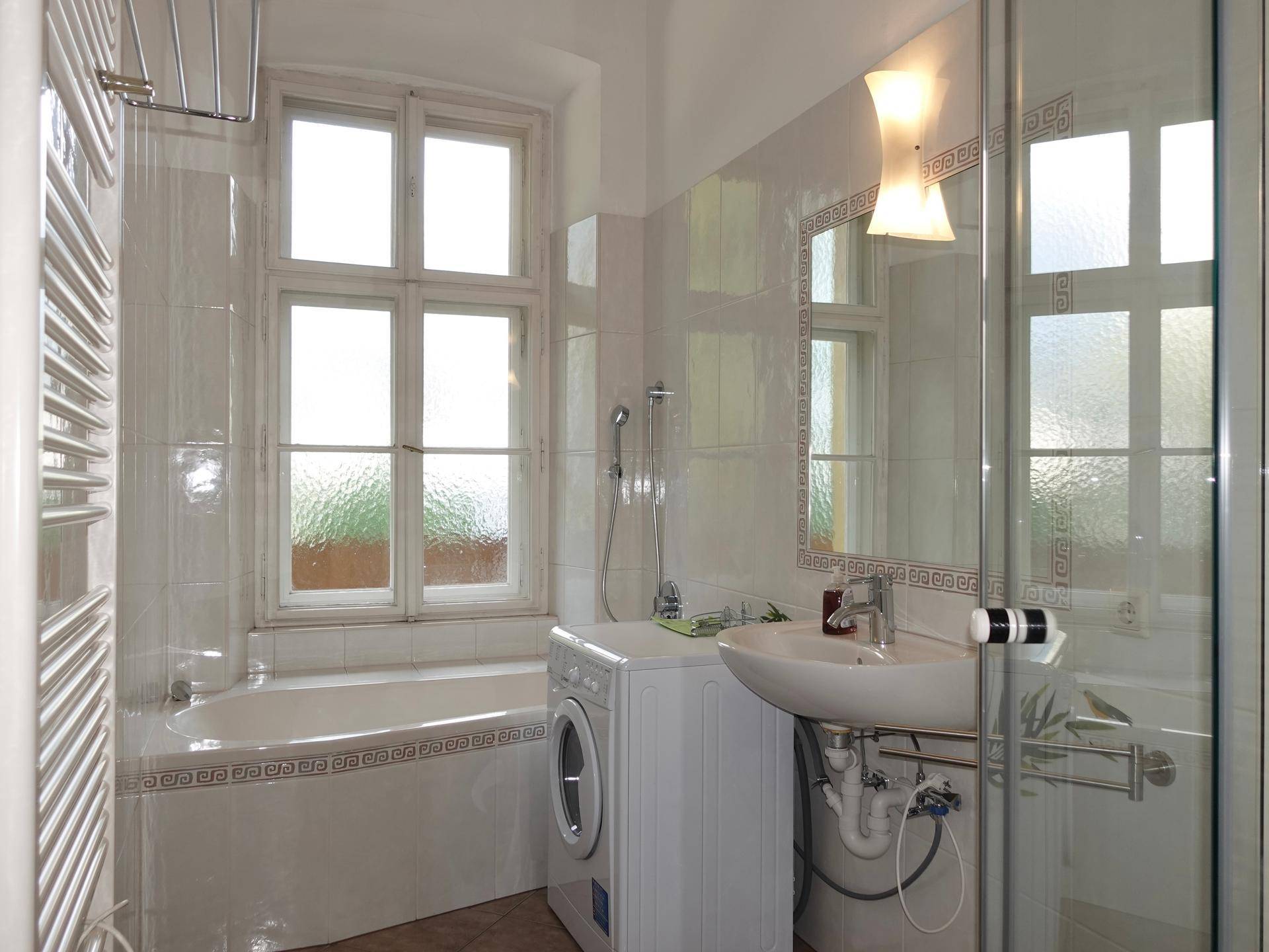 Helles Badezimmer mit Badewanne, Dusche, Waschmaschine und Fenster, alles in hellen Fliesen.