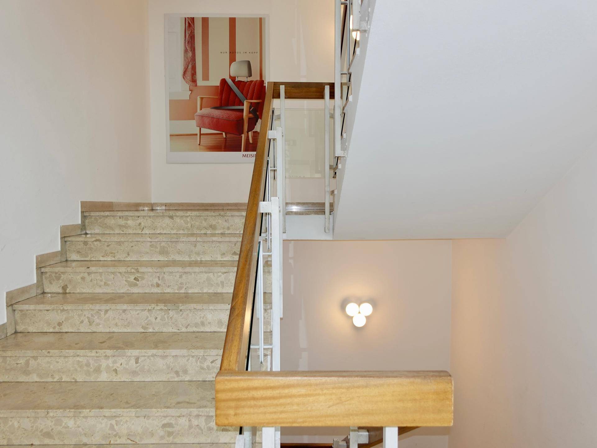 Treppenhaus mit Marmorstufen, Holzgeländer und einem dekorativen Bild an der Wand.
