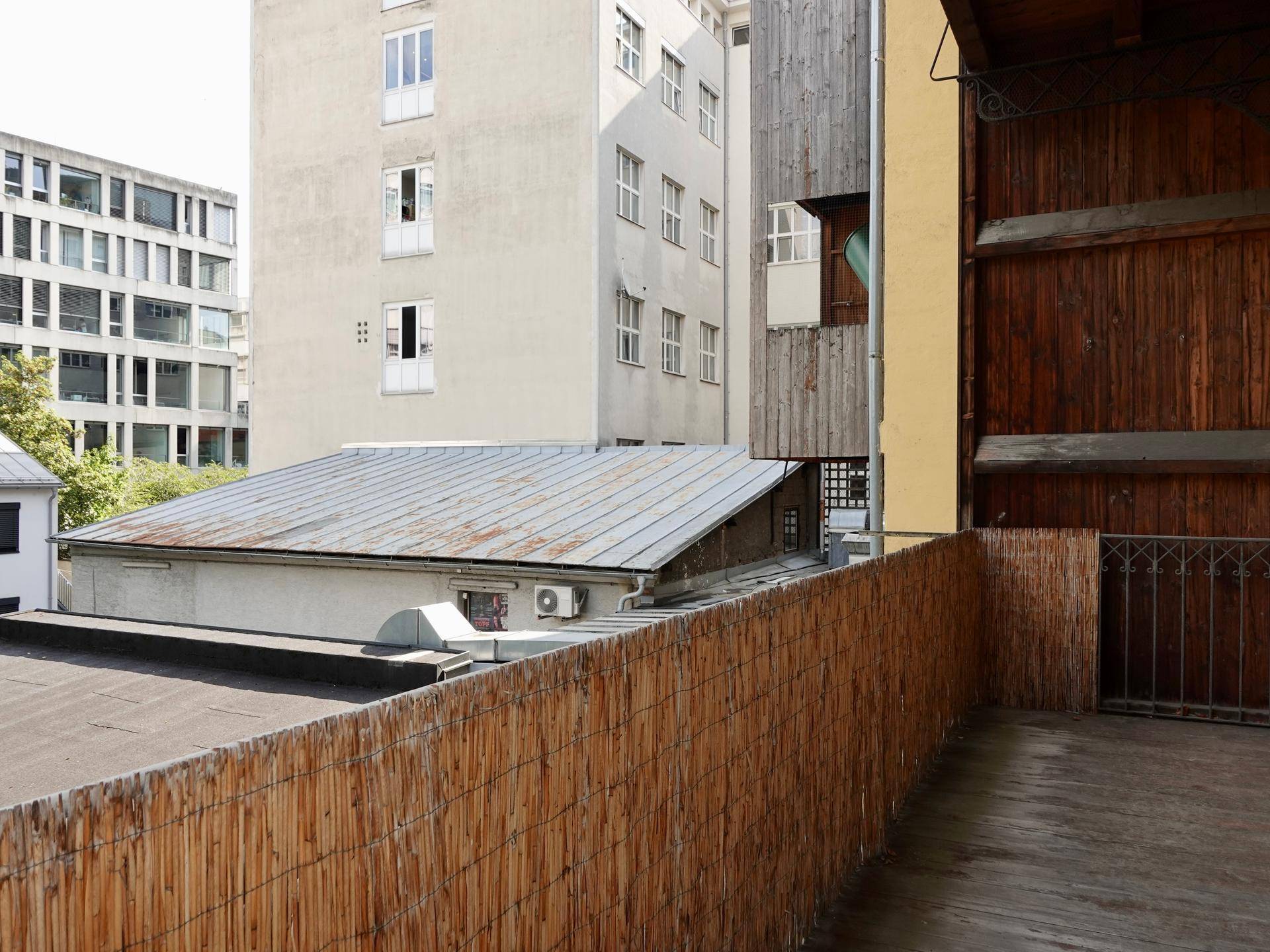 Blick von einem Balkon auf umliegende Gebäude und Dächer, mit einem Bambuszaun im Vordergrund.