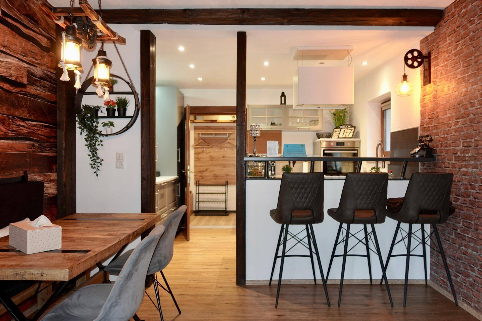 Rustikaler Essbereich mit Holztisch, Backsteinwand und Blick in die moderne Küche.