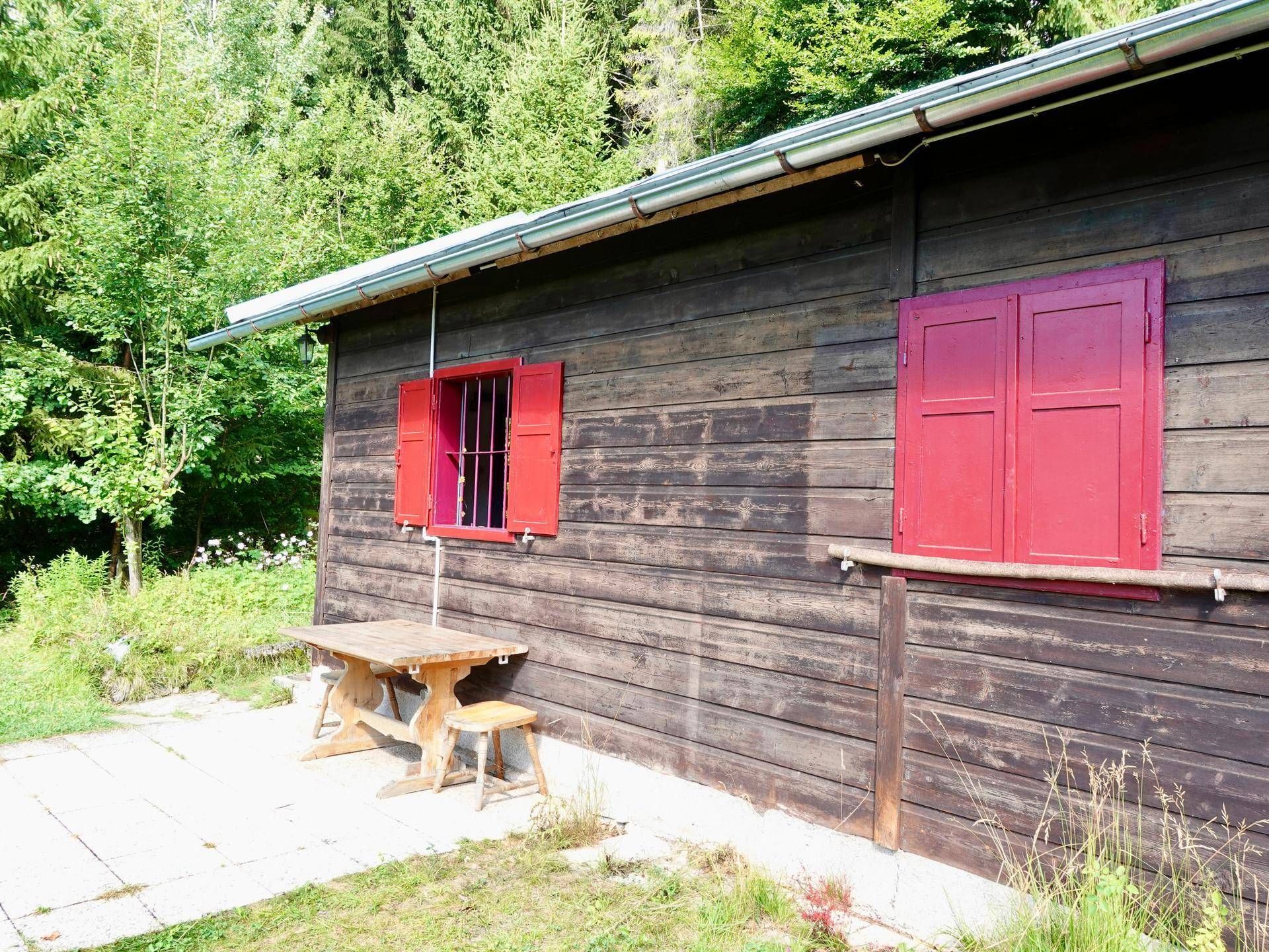 Rustikale Terrasse mit Holztisch und Sitzbank vor der Holzhütte, umgeben von Natur.