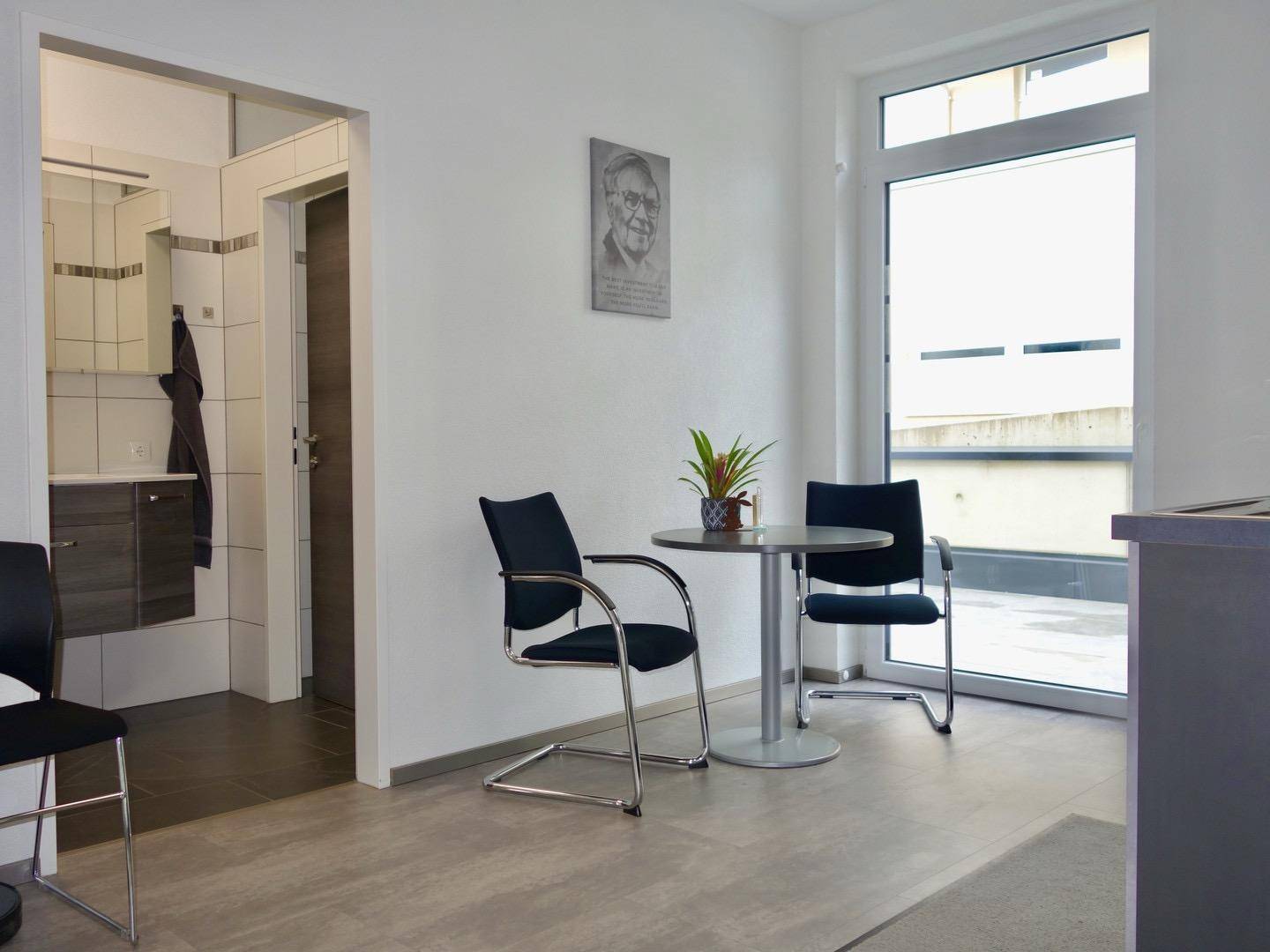 Gemütlicher Wartebereich mit kleinem Tisch und Stühlen, angrenzend an einen modernen Sanitärbereich.