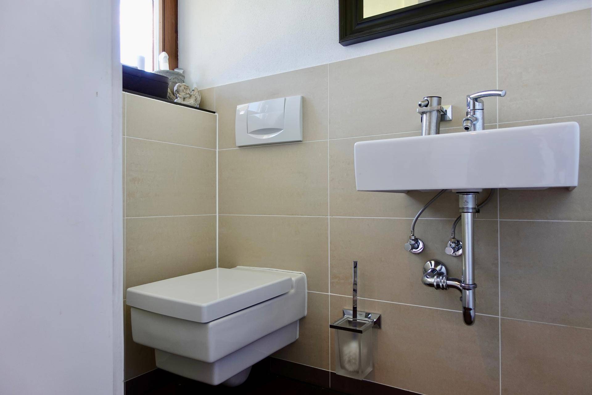 Kleines Gäste-WC mit Wand-WC und modernem Waschbecken, in neutralen Farbtönen gehalten.