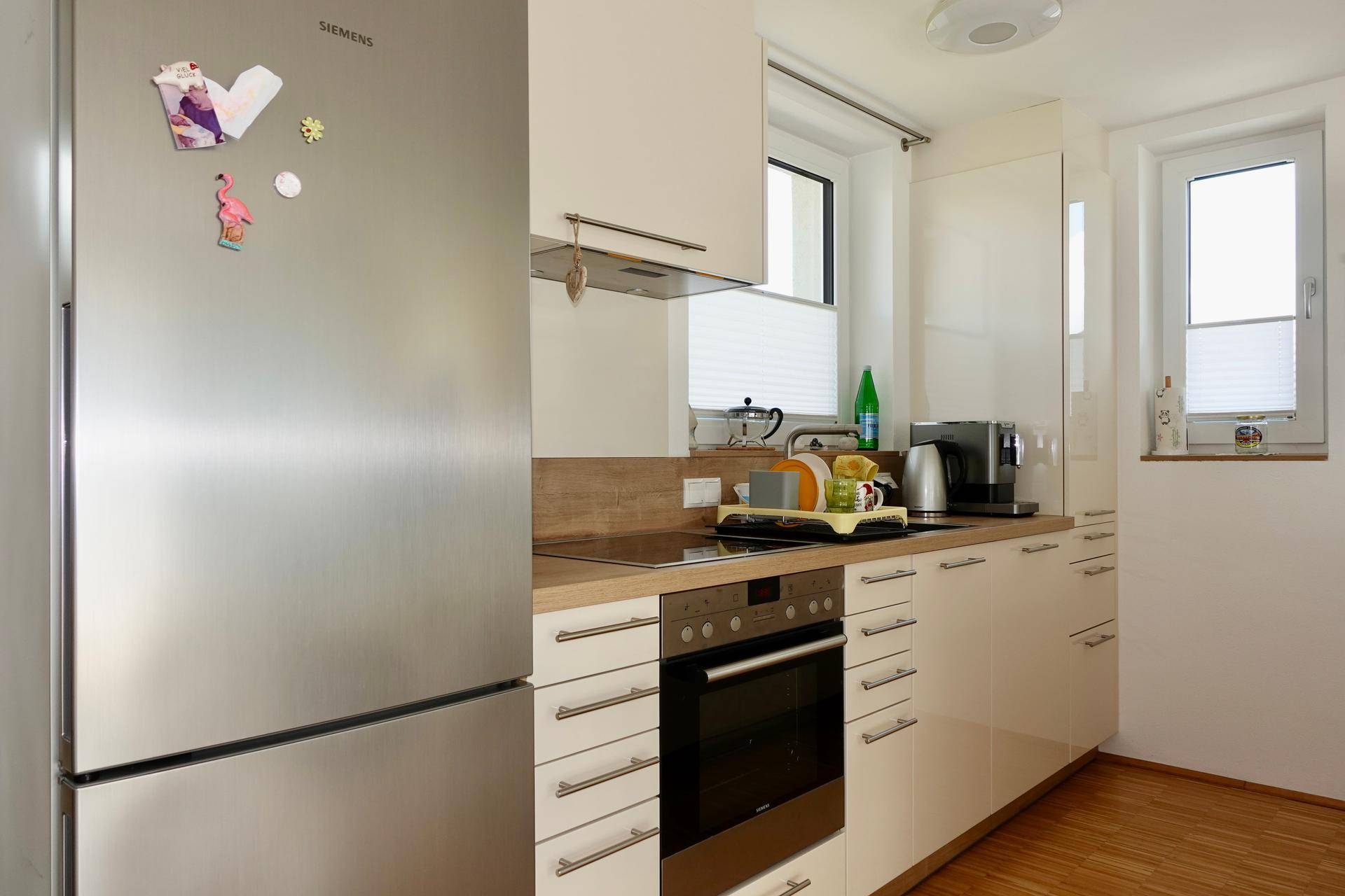 Moderne Küche mit weißen Schränken, Holzarbeitsplatte, Einbauofen und Siemens Kühlschrank.