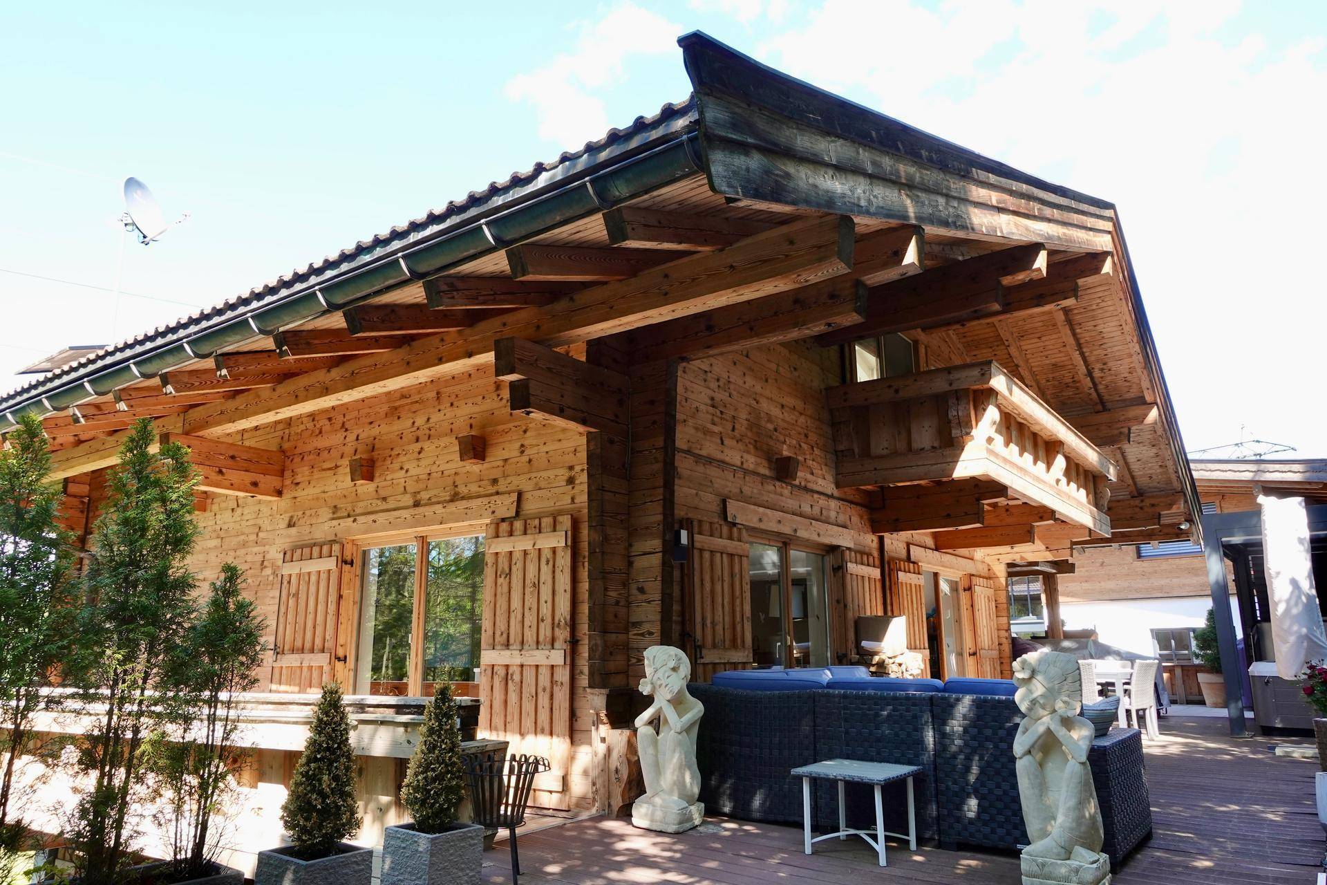 Holzverkleidetes Haus mit großer Terrasse, Whirlpool und Skulpturen im Außenbereich.
