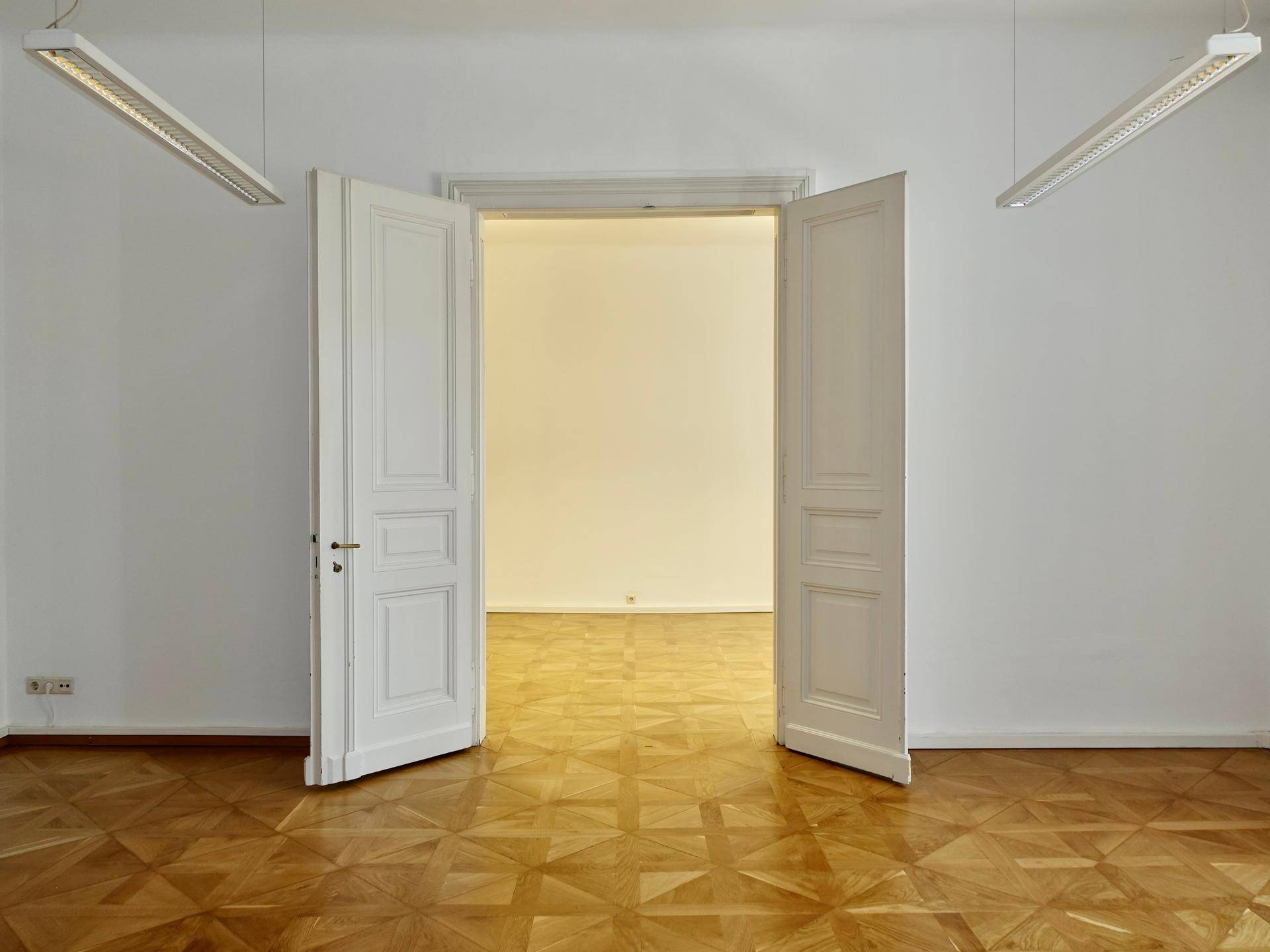 Geräumiger Raum mit Fischgrätparkett und hohen Doppeltüren, die zu einem weiteren Zimmer führen.